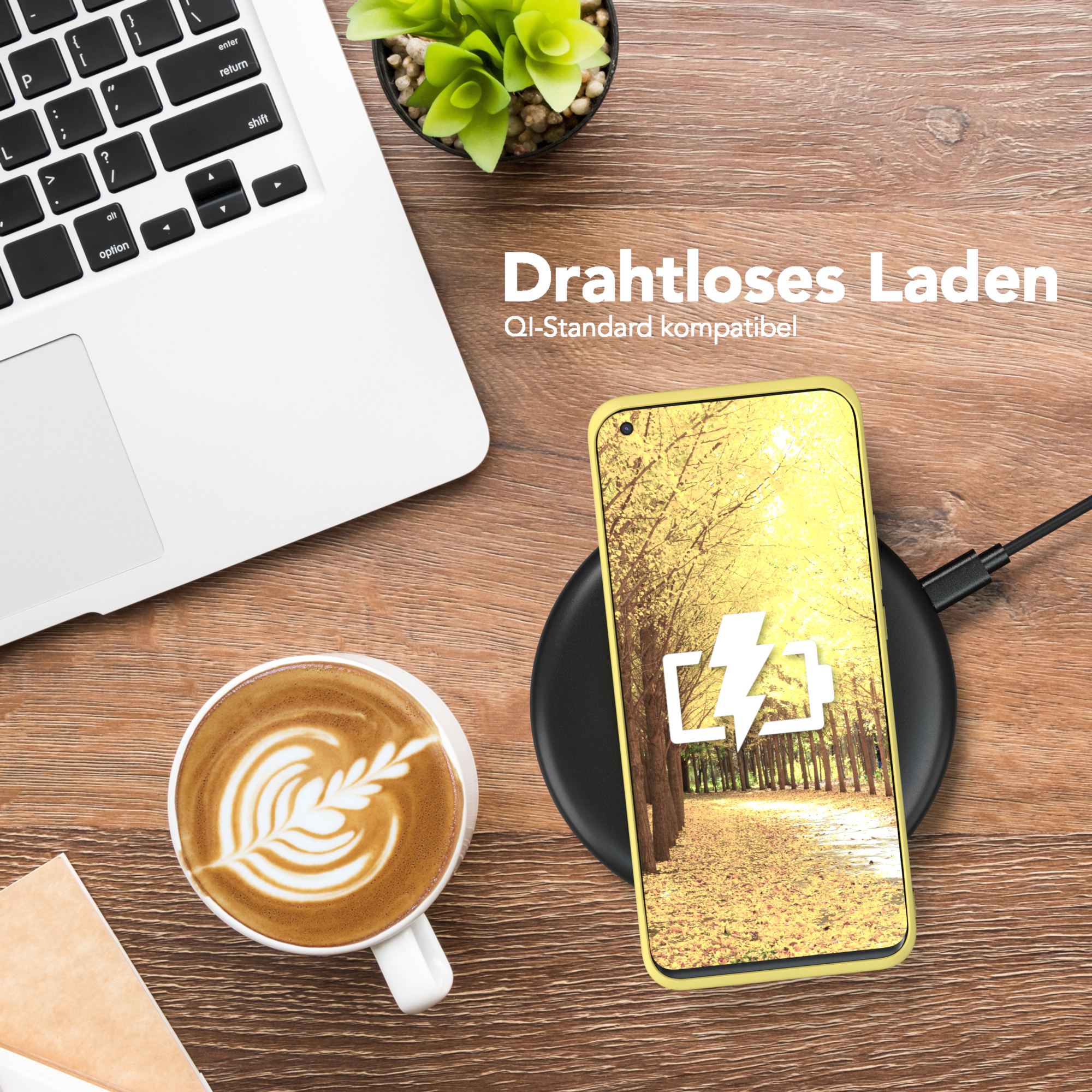 Ein Telefon auf einem kabellosen Ladegerät neben einem Laptop und einer Tasse Kaffee mit Latte Art auf einem Holztisch.
