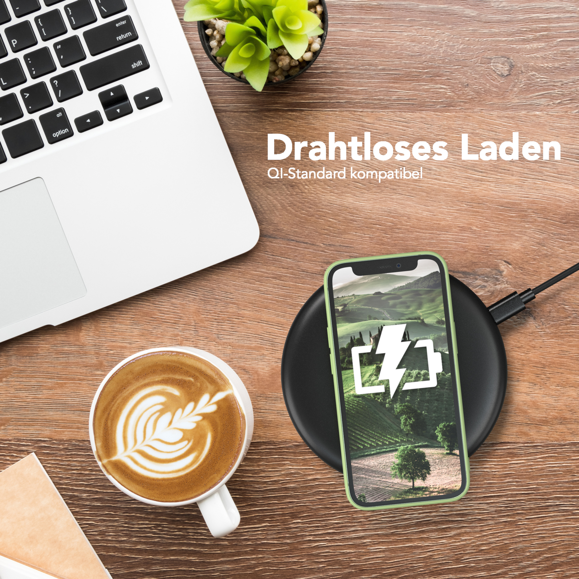 Telefon, das auf einem schwarzen kabellosen Ladegerät geladen wird, ein Laptop, Kaffee und eine Pflanze auf einem Holztisch.