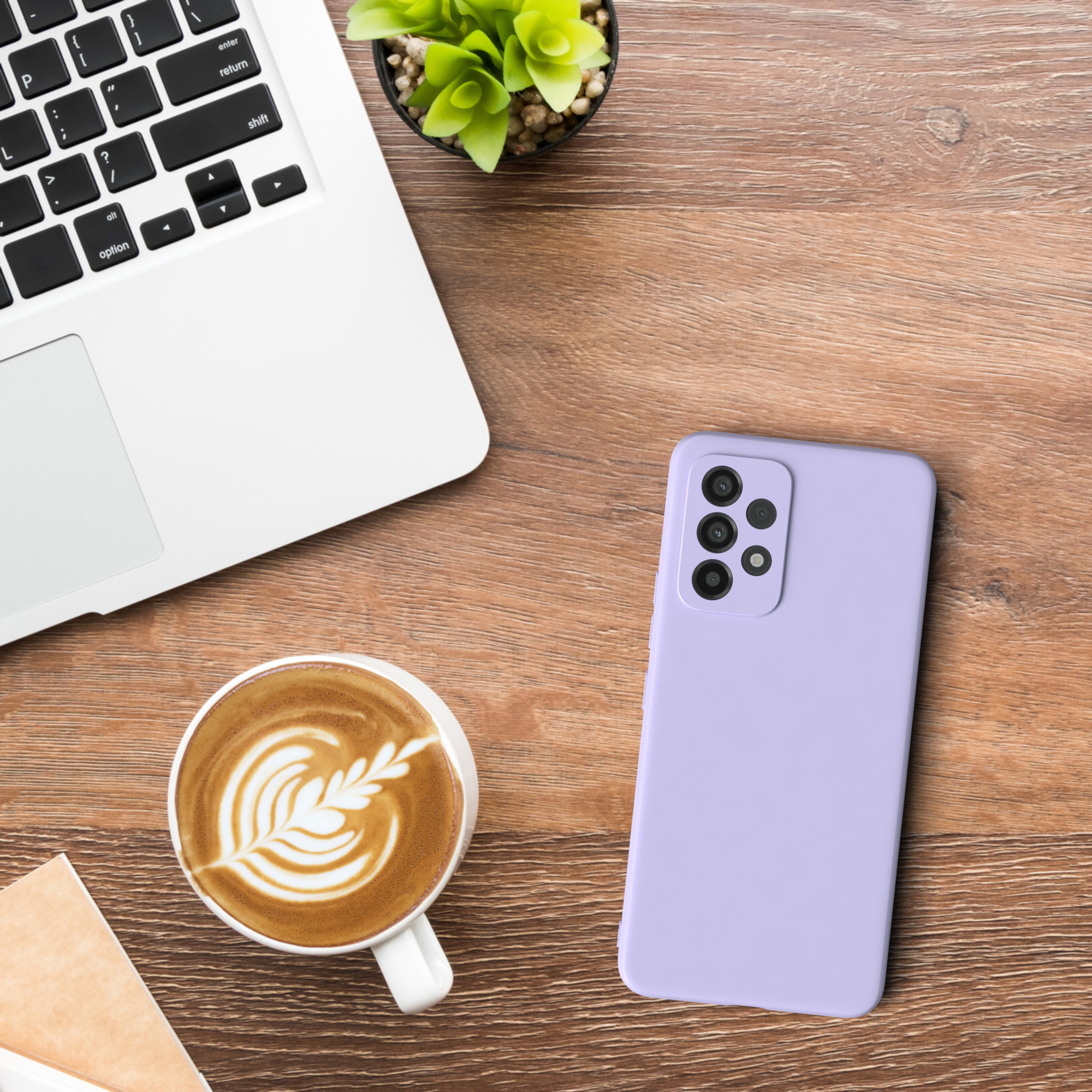 Draufsicht: Laptop, Kaffee mit Latte Art, Pflanze und eine lavendelfarbene Handyhülle auf einem Holztisch.