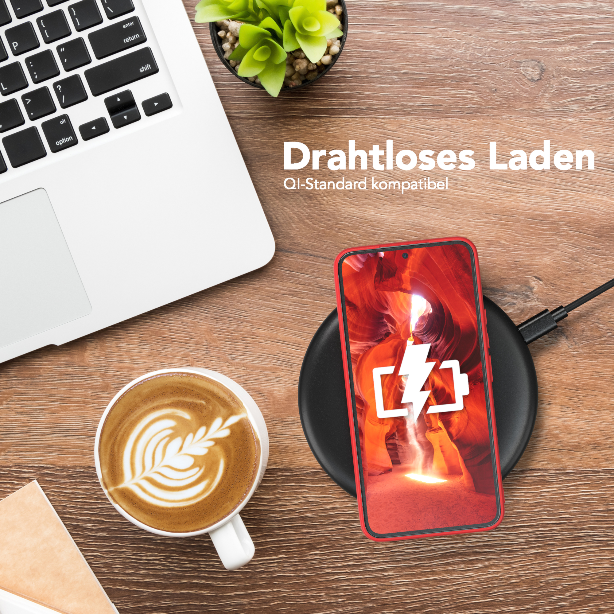 Ein Telefon, das auf einem kabellosen Ladegerät geladen wird, neben einem Laptop und einer Kaffeetasse. Holz-Hintergrund.