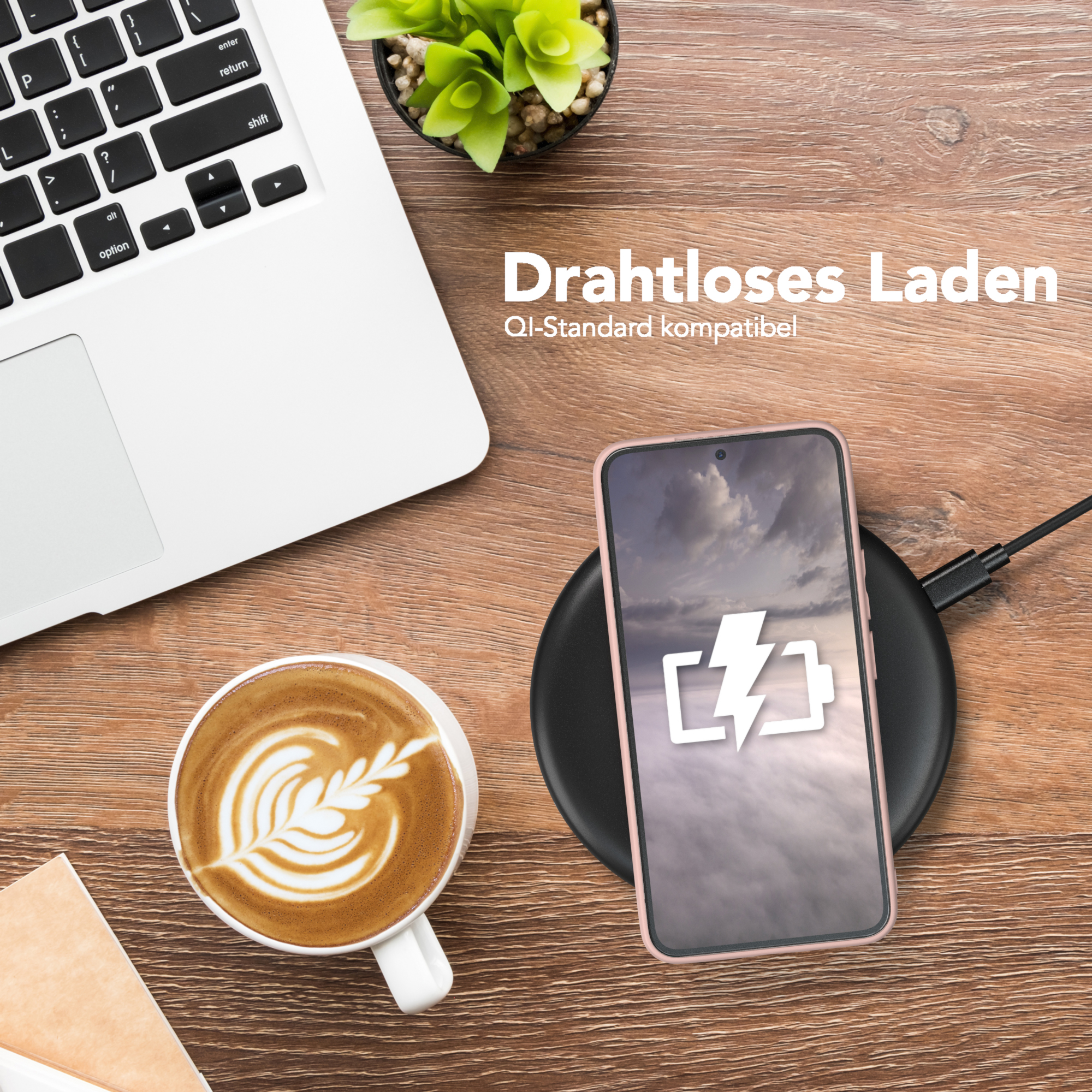 Ein Telefon, das drahtlos auf einem schwarzen Pad geladen wird, neben einem Laptop und einer Kaffeetasse. Holztisch.