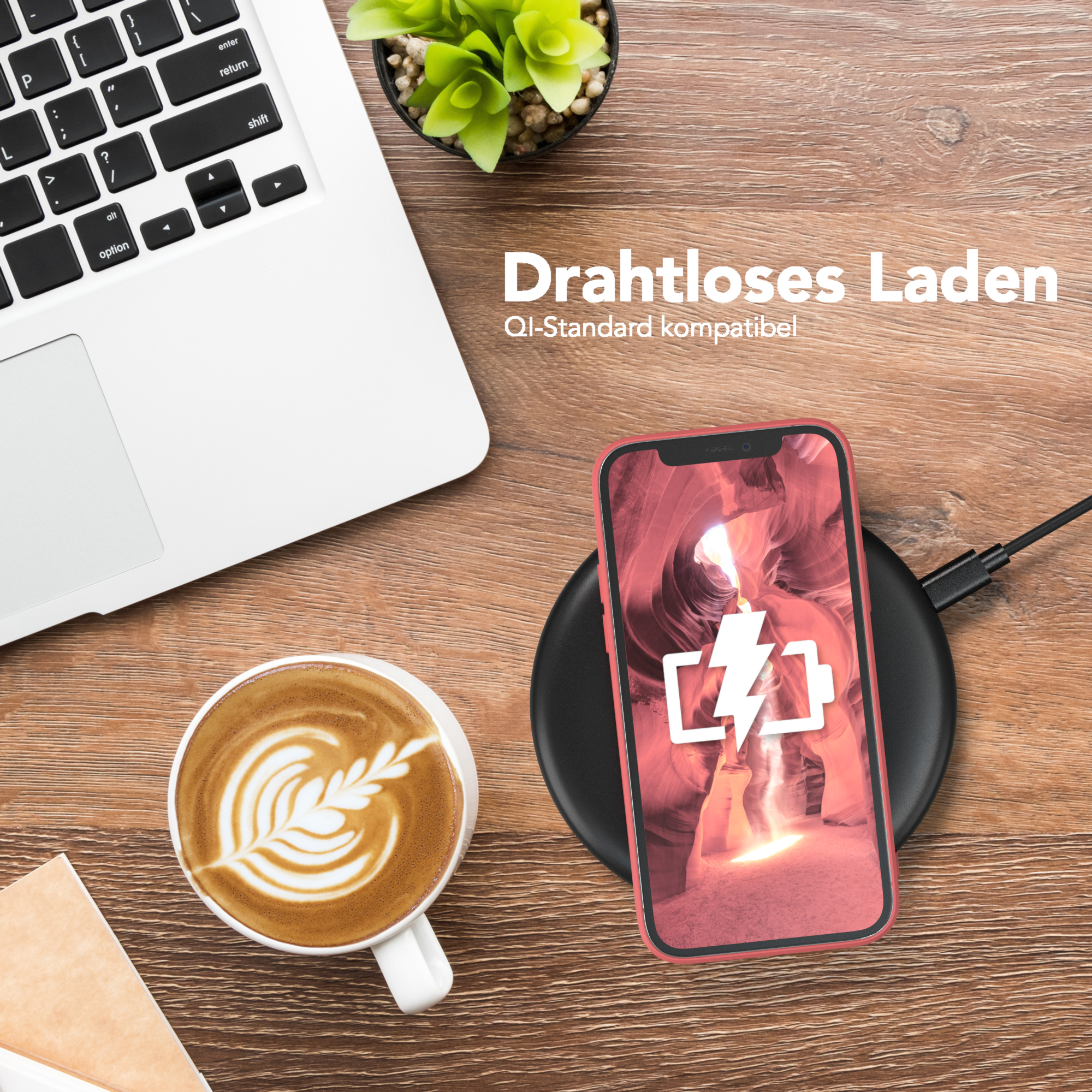 Ein Handy auf einem kabellosen Ladegerät neben einem Laptop, einer Kaffeetasse und einer Pflanze auf einem Holztisch.