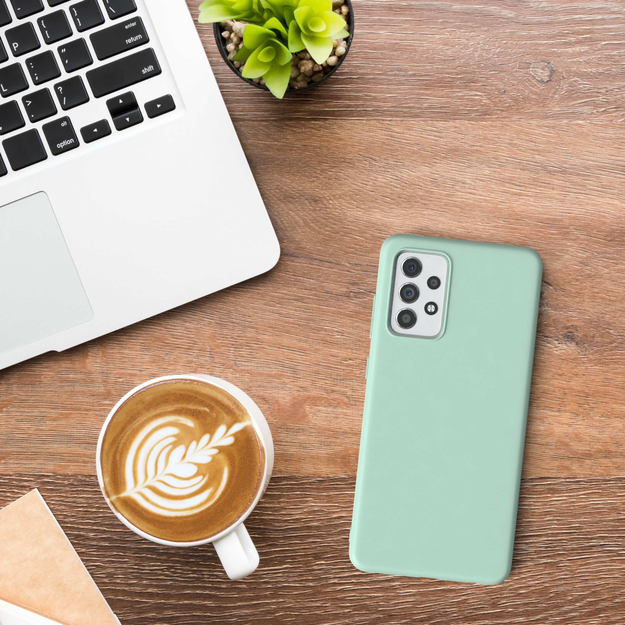 Ein Laptop, eine Kaffeetasse mit Kunst darauf und eine Handyhülle auf einem Holztisch.
