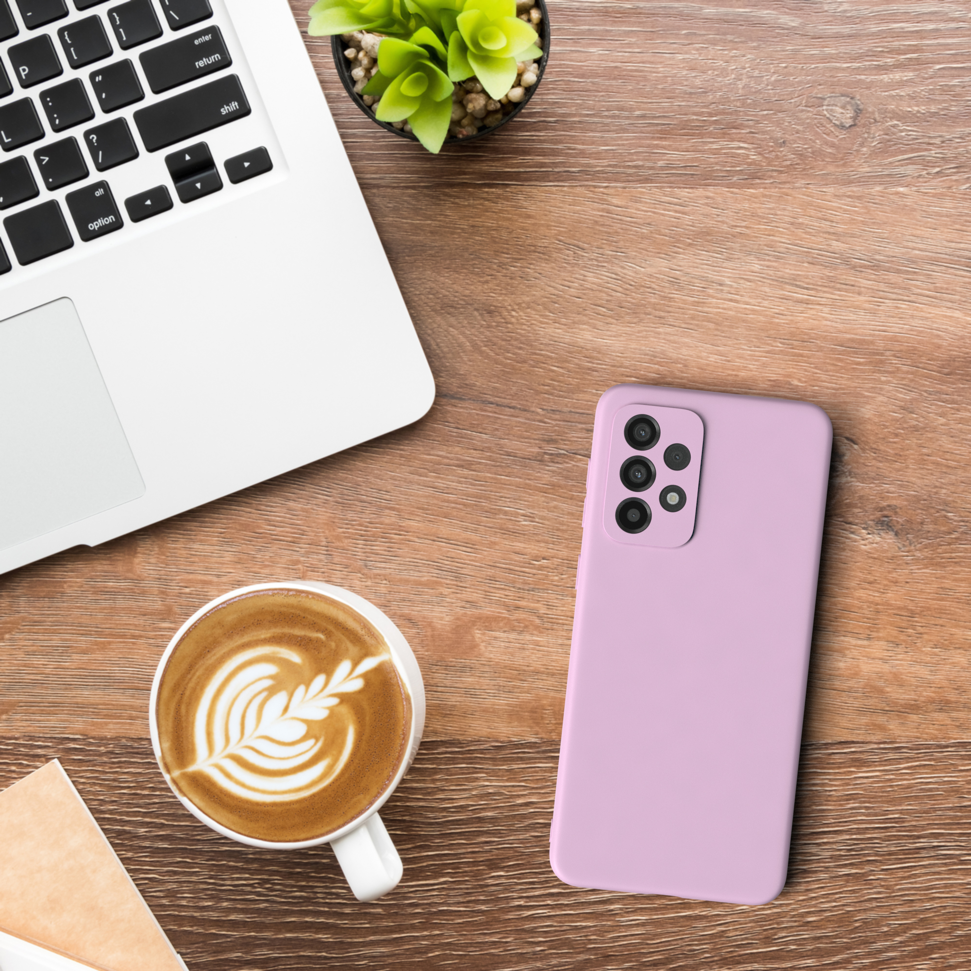 Laptop, Kaffee, Pflanze und eine Handyhülle auf einem Holztisch. Handyhülle ist pink.