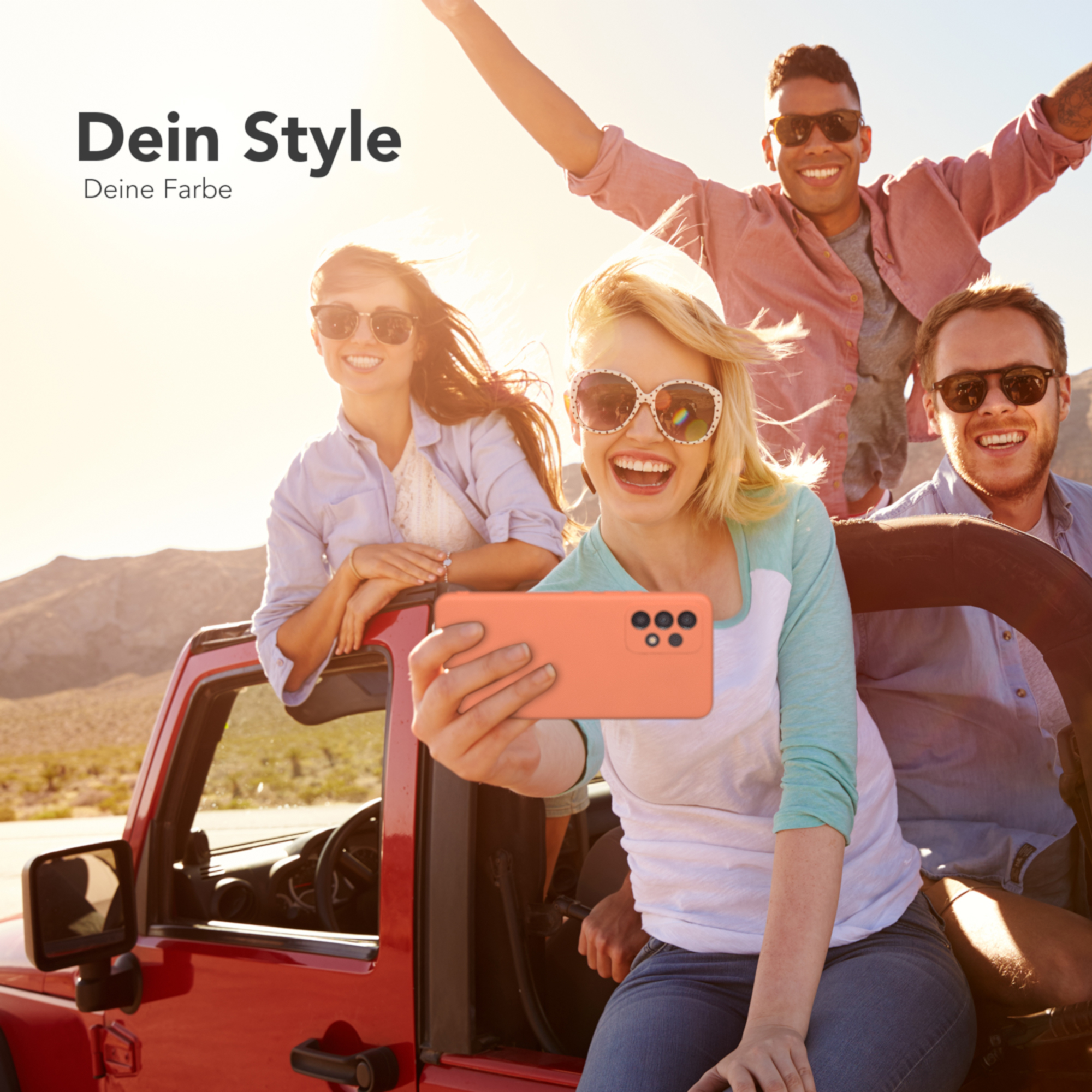 Vier Personen in einem roten Jeep machen ein Selfie. Sie lächeln mit einem Wüstenhintergrund.