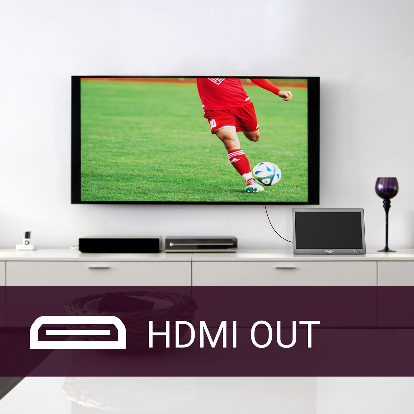 Un televisor muestra un partido de fútbol. Abajo hay un televisor, un altavoz y un artículo decorativo.