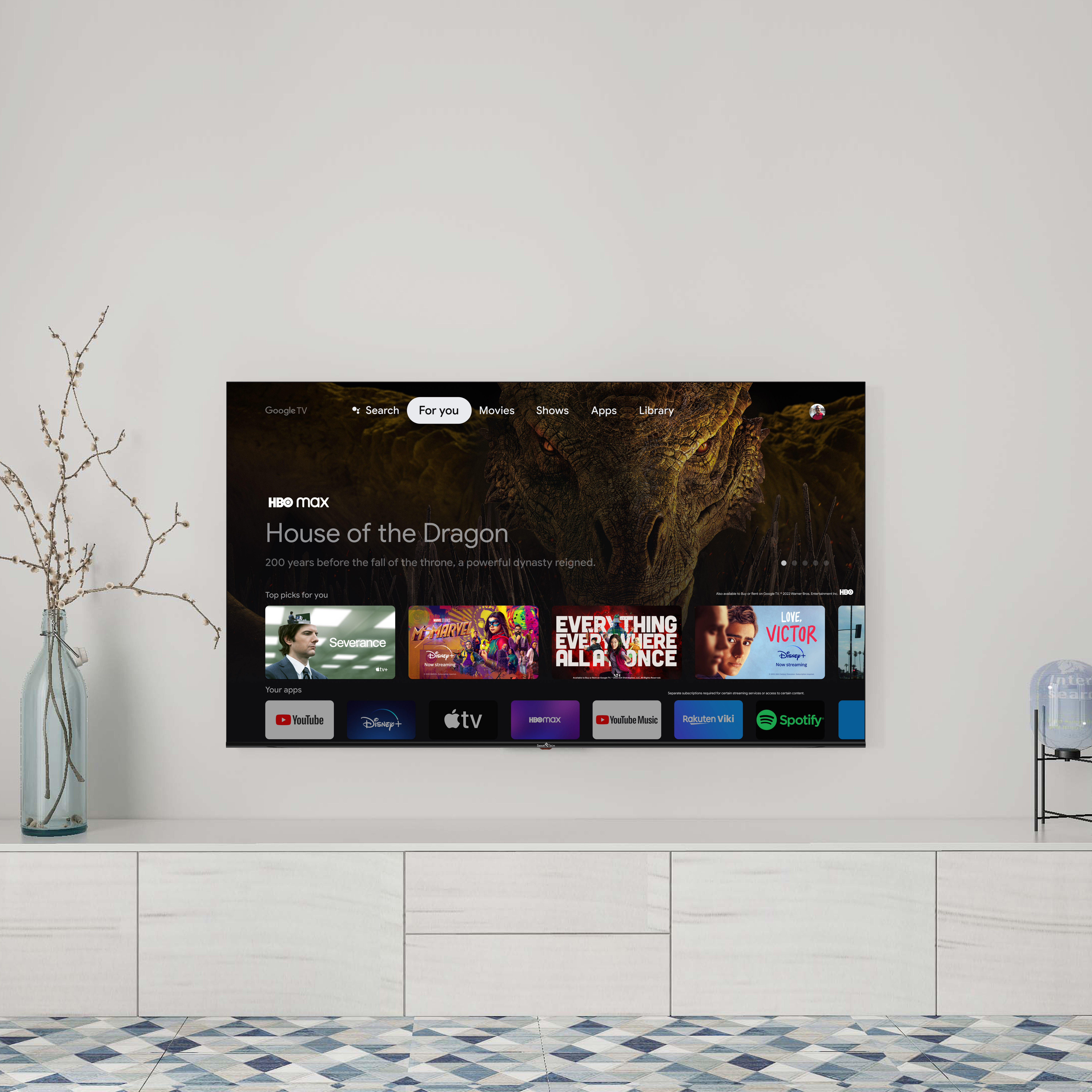 Un grande schermo TV che mostra l'interfaccia HBO Max, mostrando contenuti. Un vaso con un ramo a sinistra.