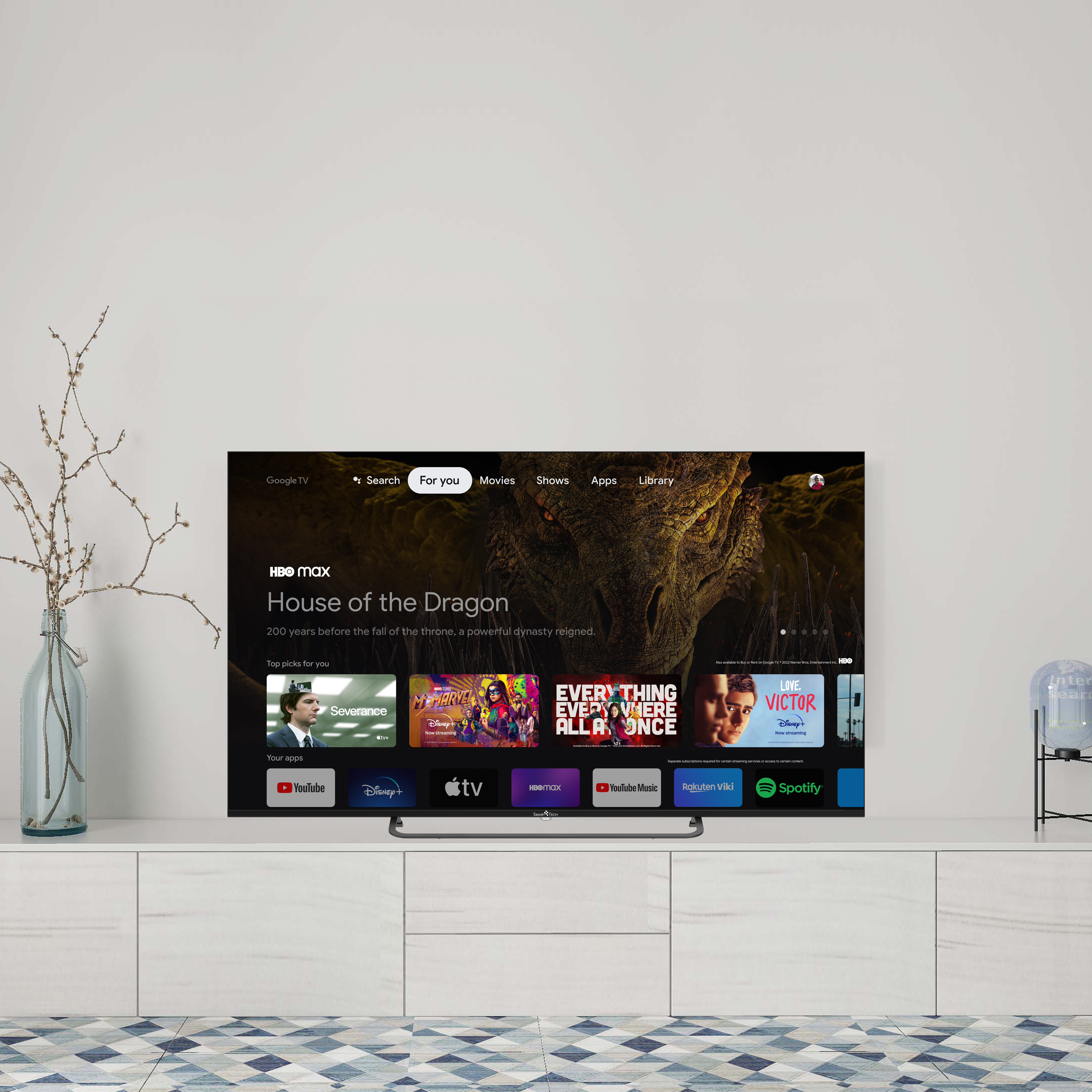 Telewizor wyświetlający usługę strumieniowania, zamontowany na białej szafce, z wazonem i dywanem.