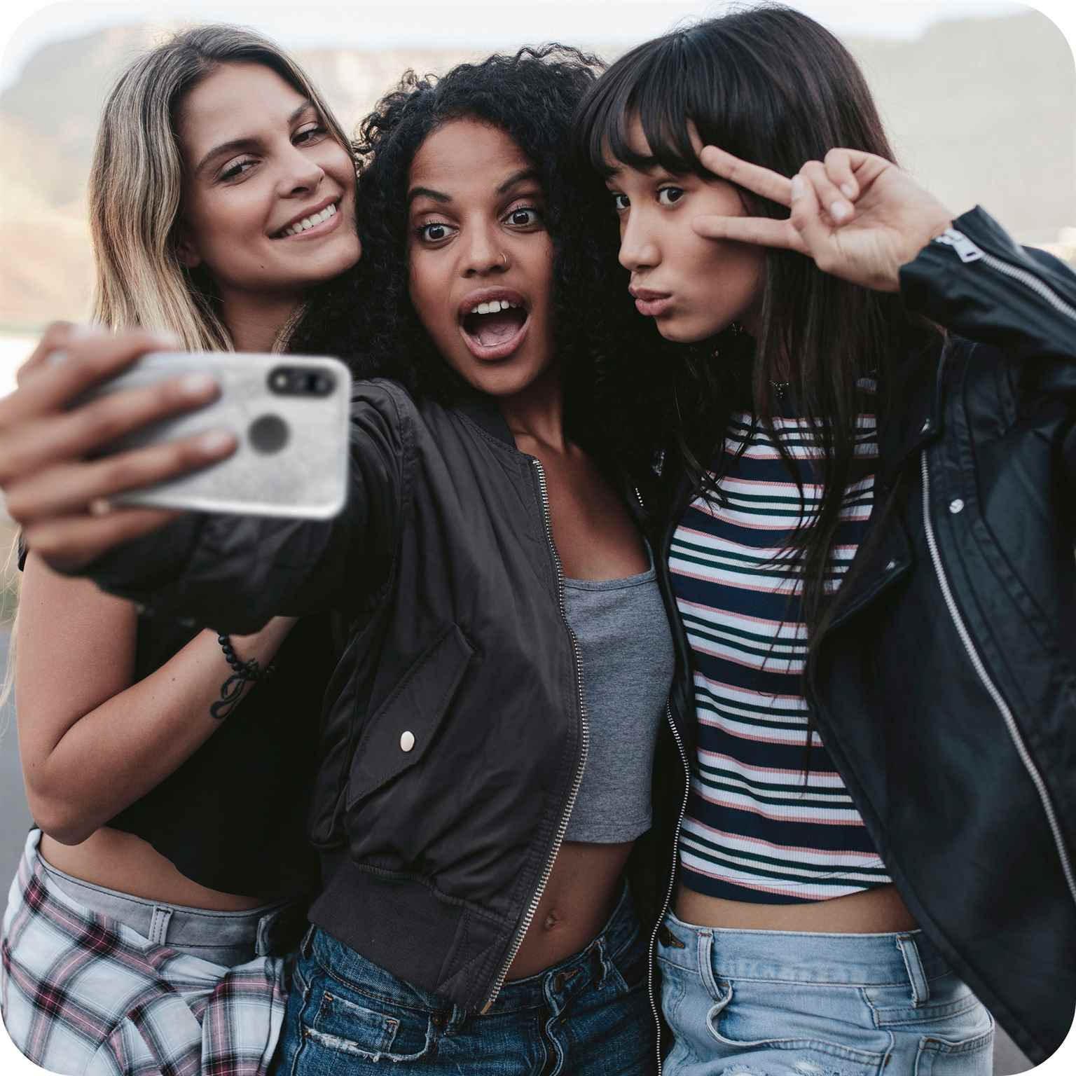 Drei Frauen machen ein Selfie mit einem Telefon in einer transparenten Hülle. Eine macht ein Peace-Zeichen.
