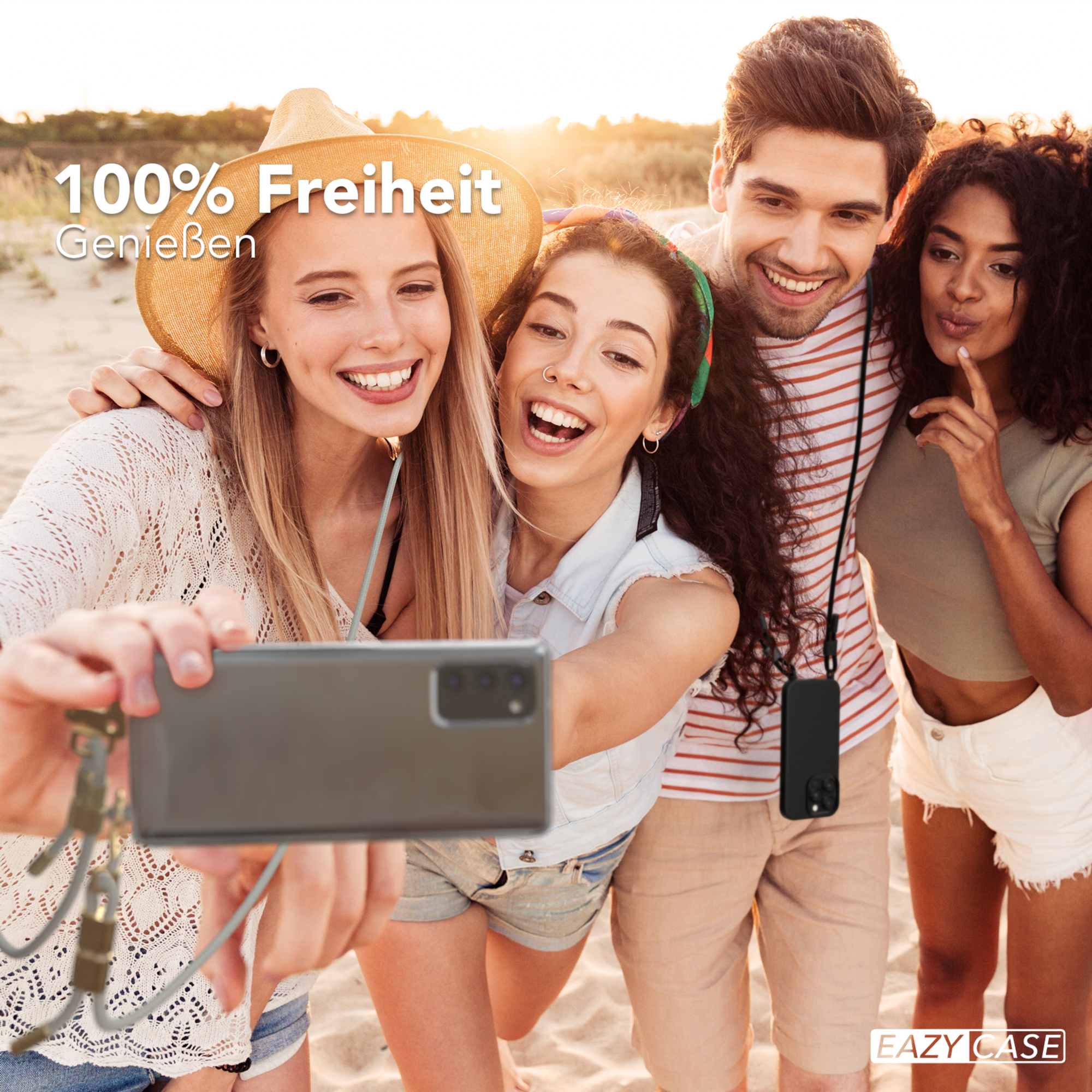 Vier Personen machen ein Selfie am Strand. Einer hält das Telefon. Sonniger Himmel und Sand im Hintergrund.