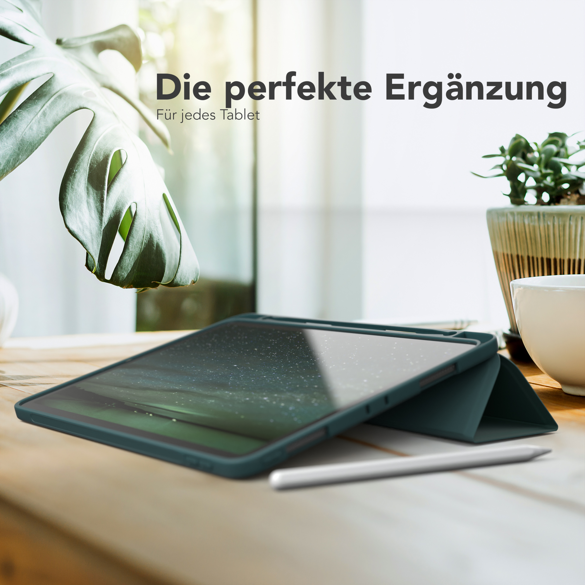 Ein Tablet in einer grünen Hülle mit einem Stift auf dem Tisch. Eine Pflanze und eine Tasse sind ebenfalls sichtbar.