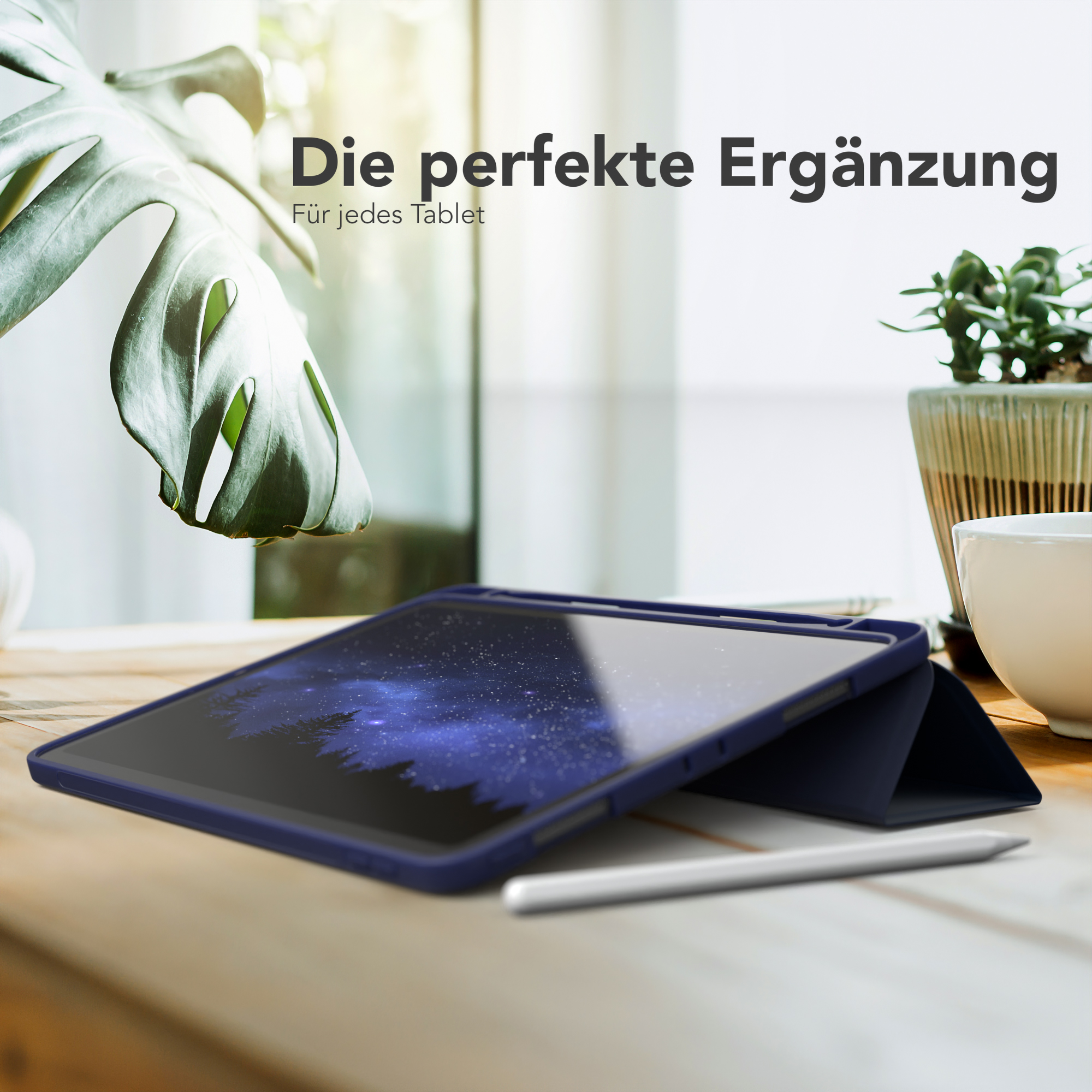 Tablet in einer marineblauen Hülle auf einem Holztisch. Weißer Stift liegt auf dem Tisch. Hintergrund ist ein Fenster.