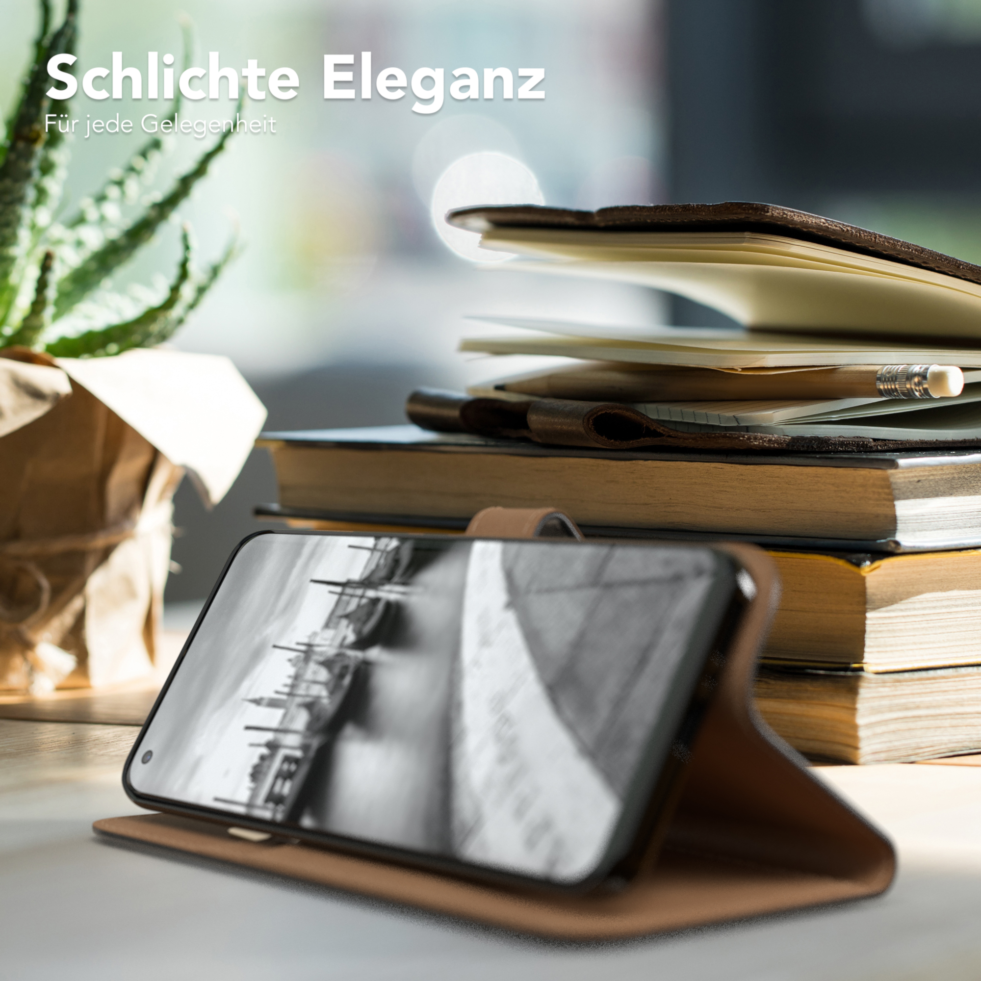 Ein Handy in einer braunen Lederhülle liegt auf einem Tisch mit Büchern, einer Pflanze und einem Bleistift.