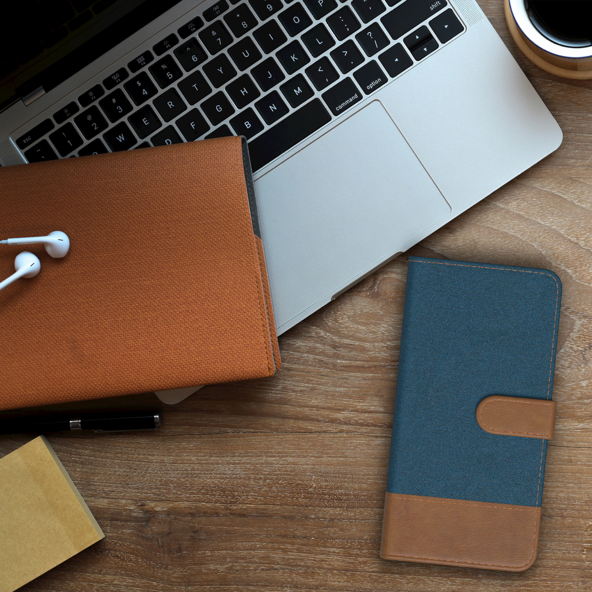 Draufsicht: Laptop, Kaffeetasse und eine Handyhülle, mit einem Notizblock und Kopfhörern.