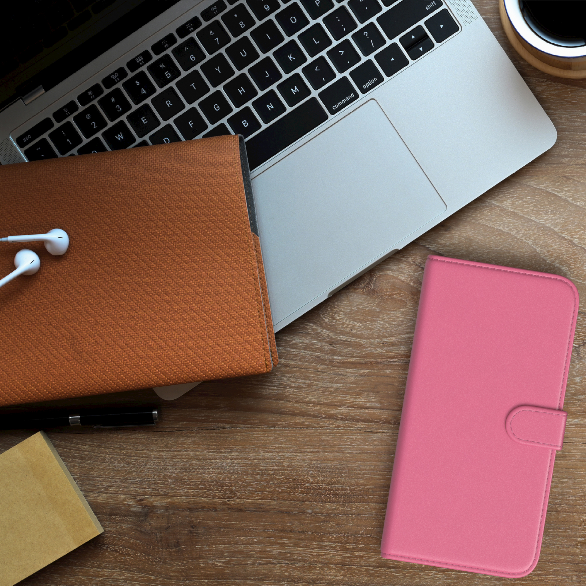 Laptop, Handyhülle, Stift und Kopfhörer auf einem Holzschreibtisch. Die Hülle ist pink.