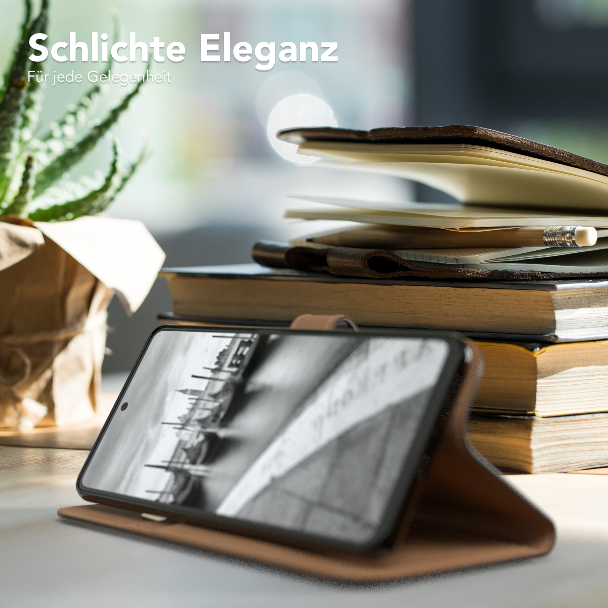 Telefon in Lederhülle auf Schreibtisch, neben Büchern und Pflanze.