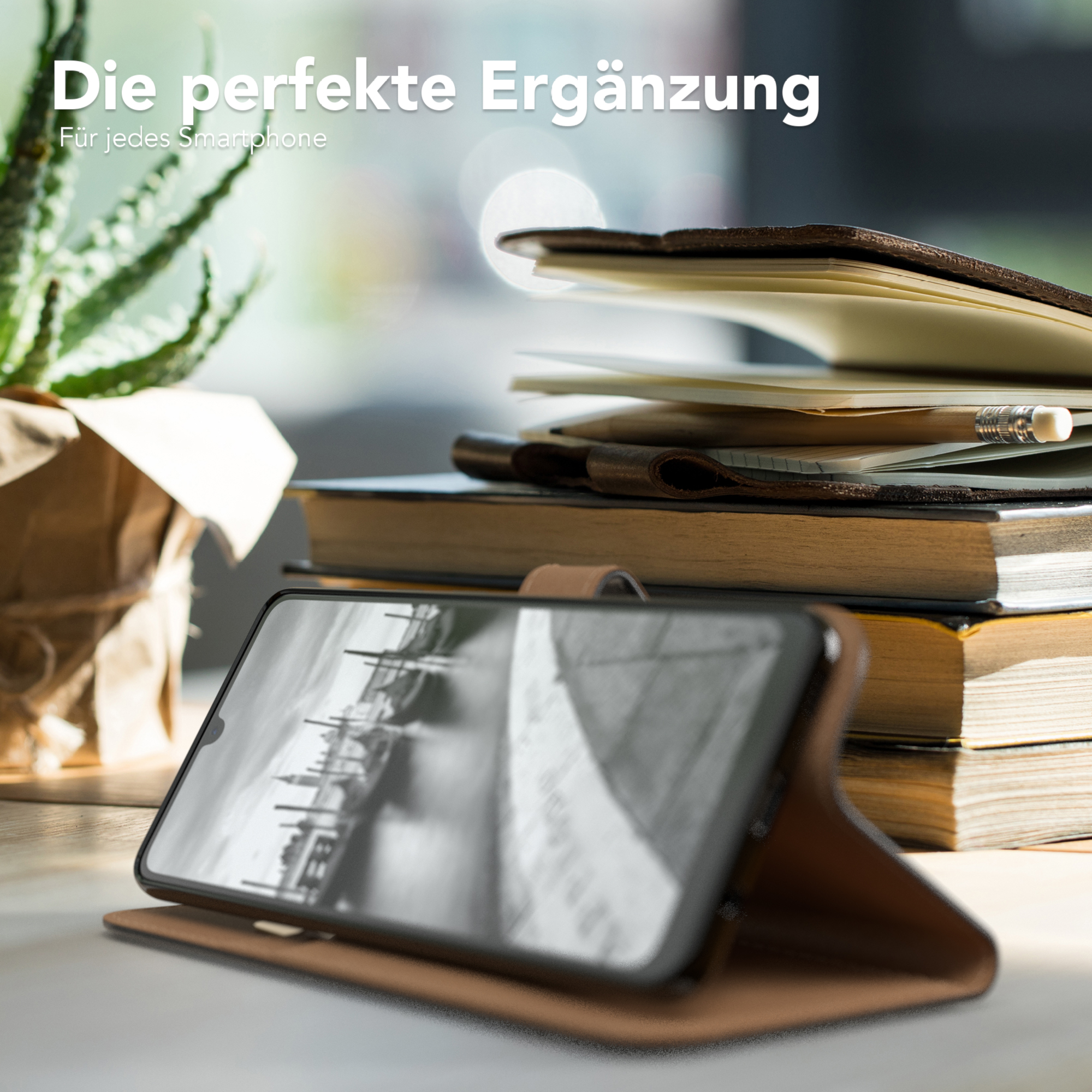 Telefon in einer Hülle auf einem Tisch mit Büchern und einer Pflanze. Text: Die perfekte Ergänzung.
