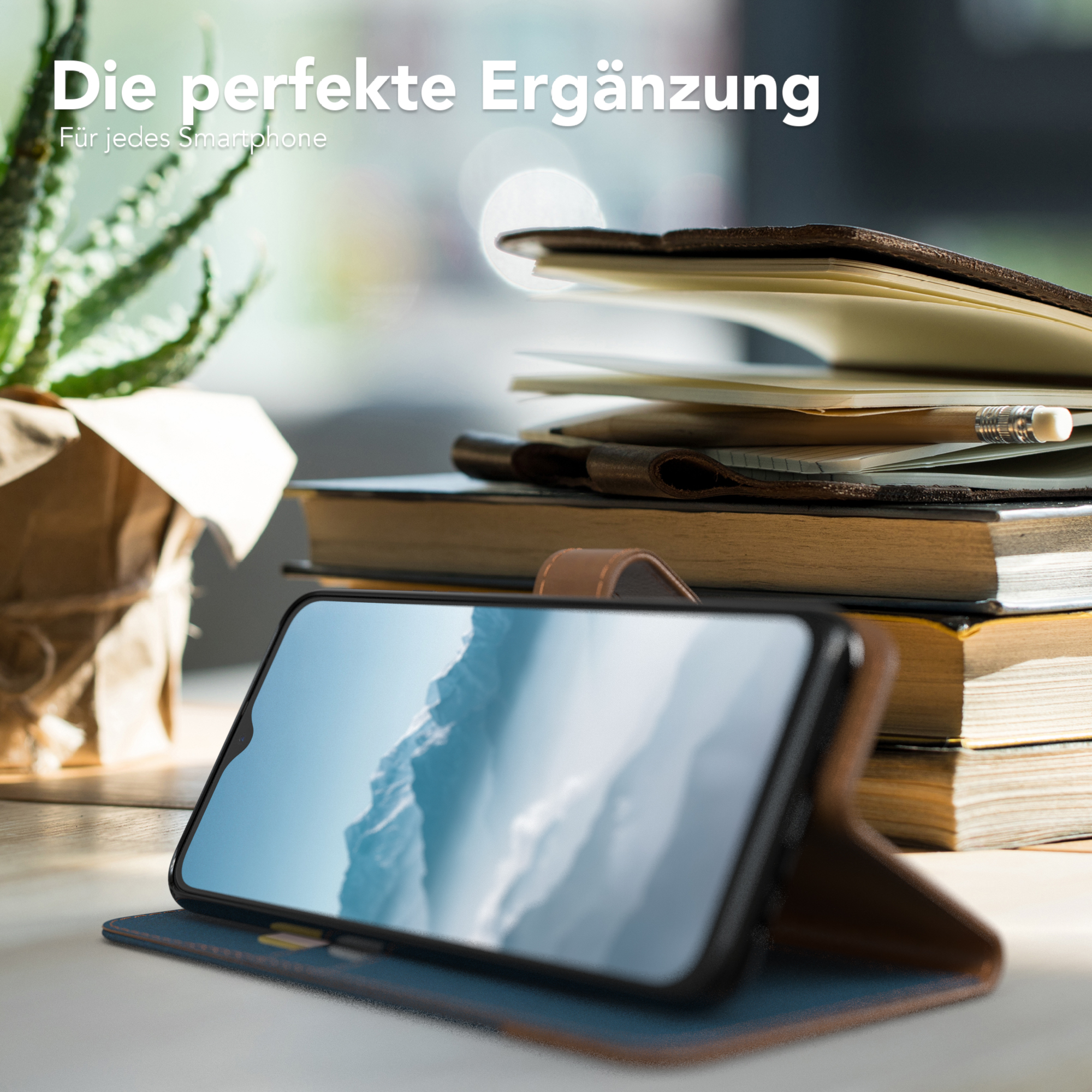 Telefon in einer Hülle auf einem Tisch mit Büchern und einer Pflanze. Text sagt "Die perfekte Ergänzung".
