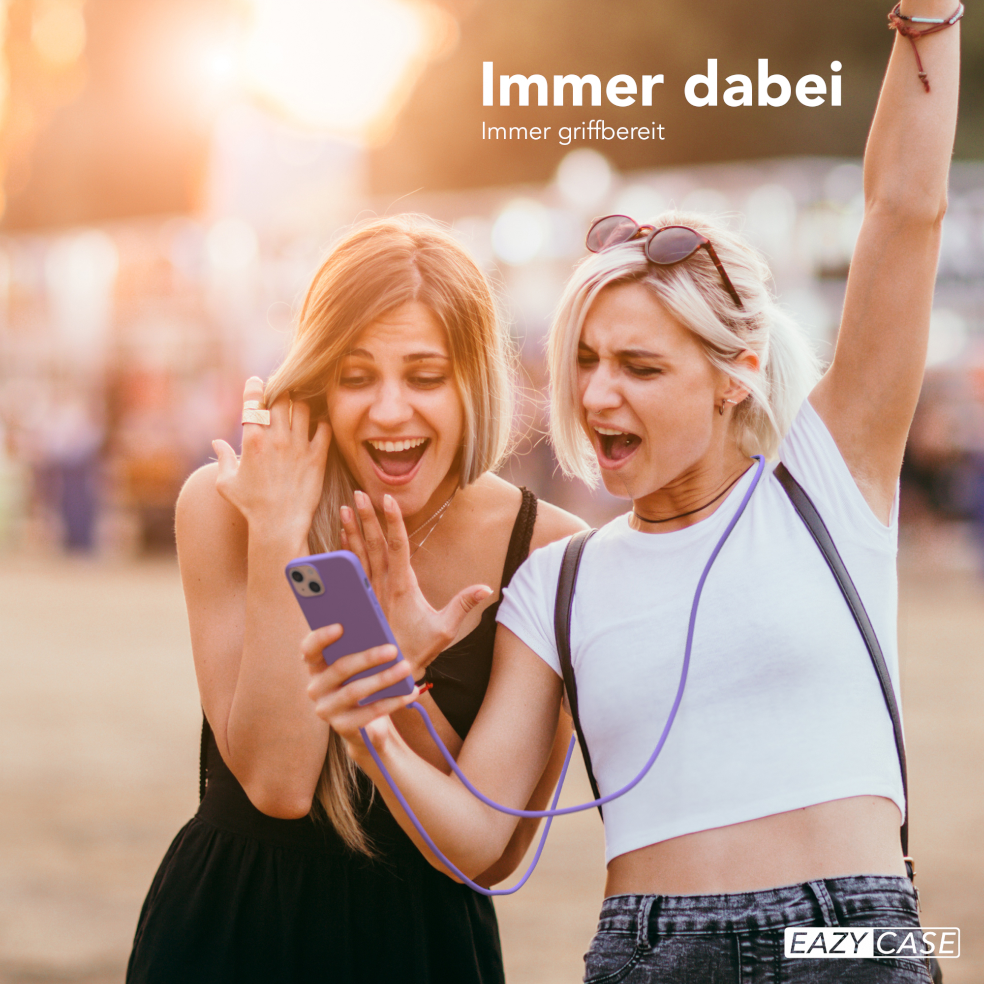 Zwei Frauen schauen sich ein Telefon mit einem Lanyard an. Sie lächeln. Es ist ein sonniger Tag.