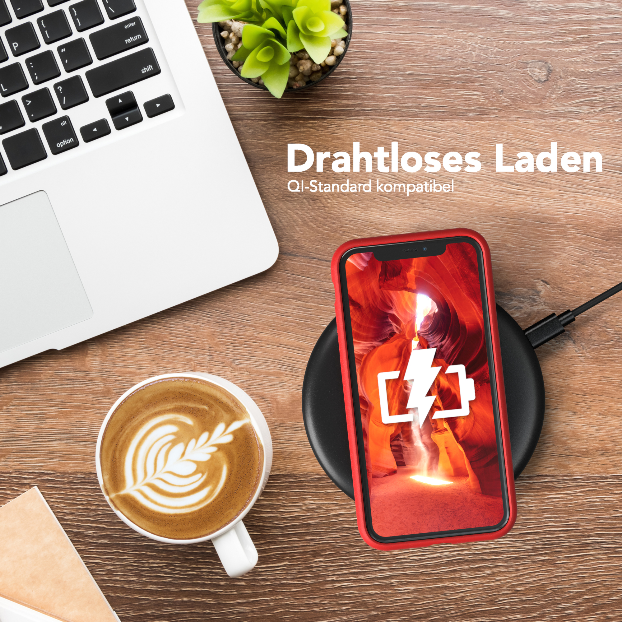 Telefon auf einem kabellosen Ladegerät, rote Handyhülle. Laptop, Kaffeetasse und Deko auf einem Holztisch. Qi-Standard kompatibel.