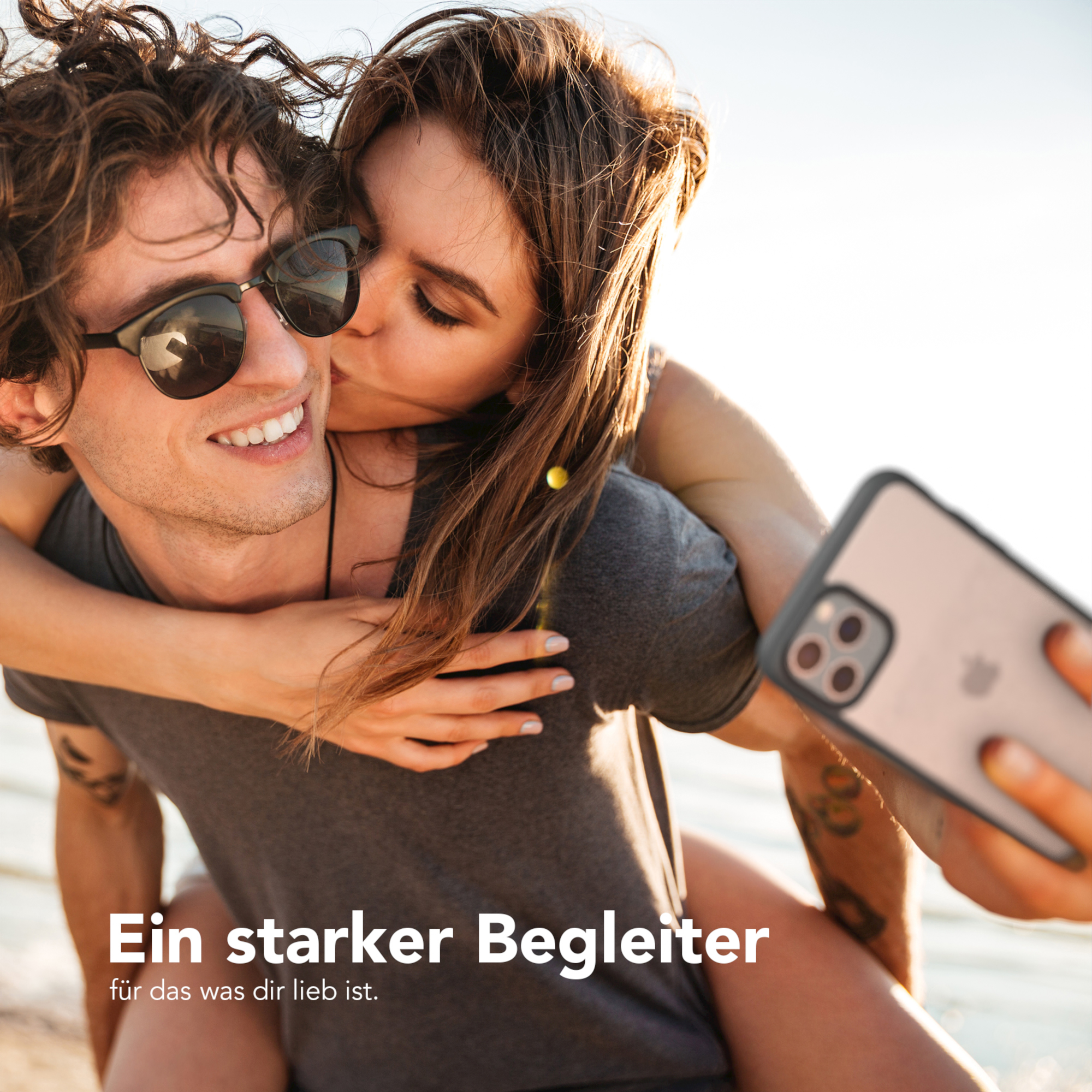Ein Paar macht ein Selfie. Die Frau küsst den Mann. Sie halten ein Telefon mit einer Hülle.