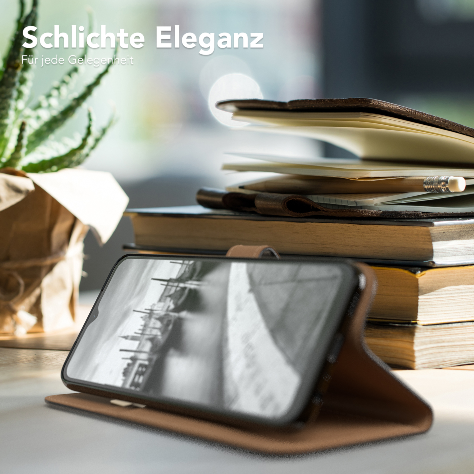 Telefon in brauner Lederhülle, auf einem Tisch. Hintergrund: Bücher, Pflanze.