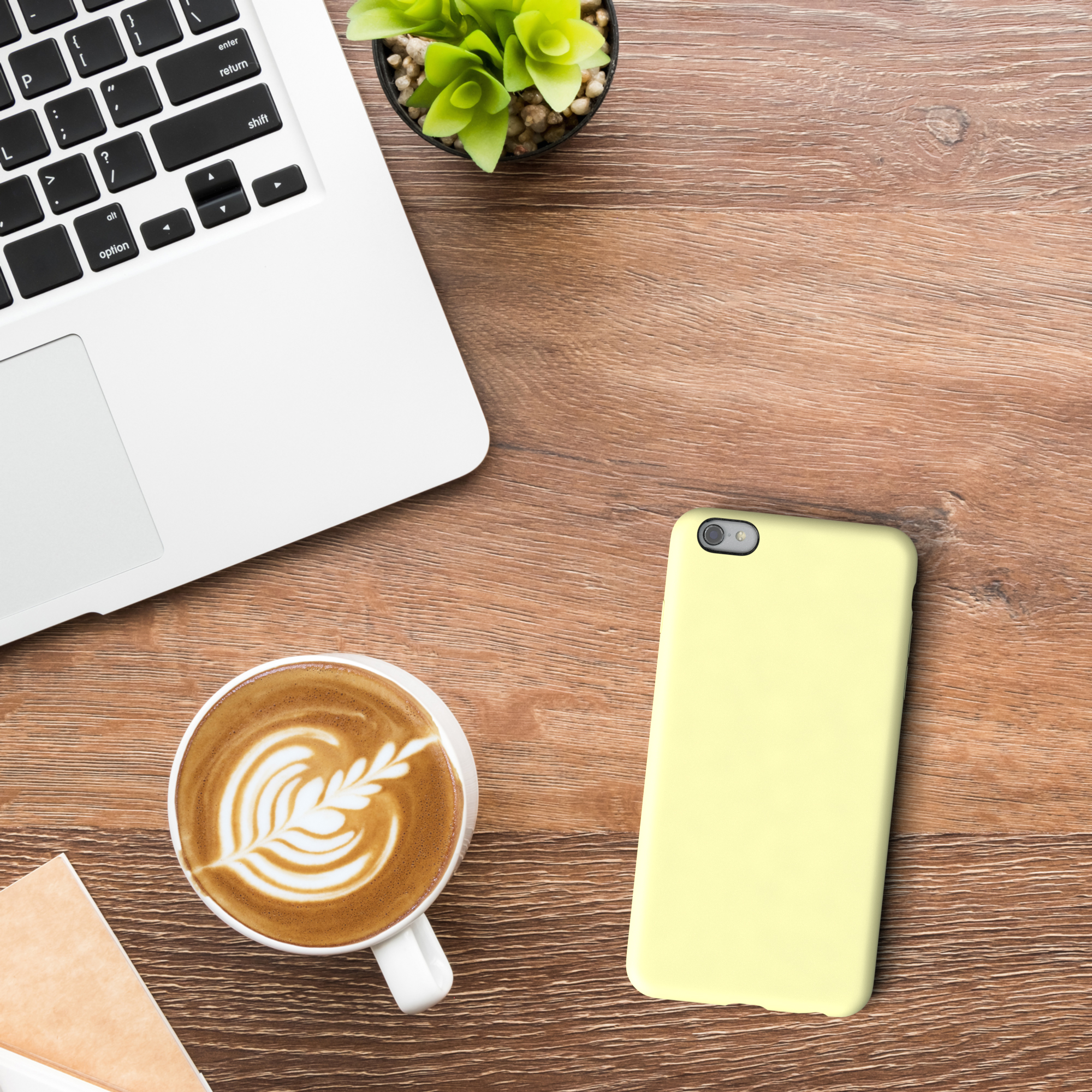 Ein Laptop, eine Kaffeetasse, ein Telefon und eine Pflanze stehen auf einem Holztisch.