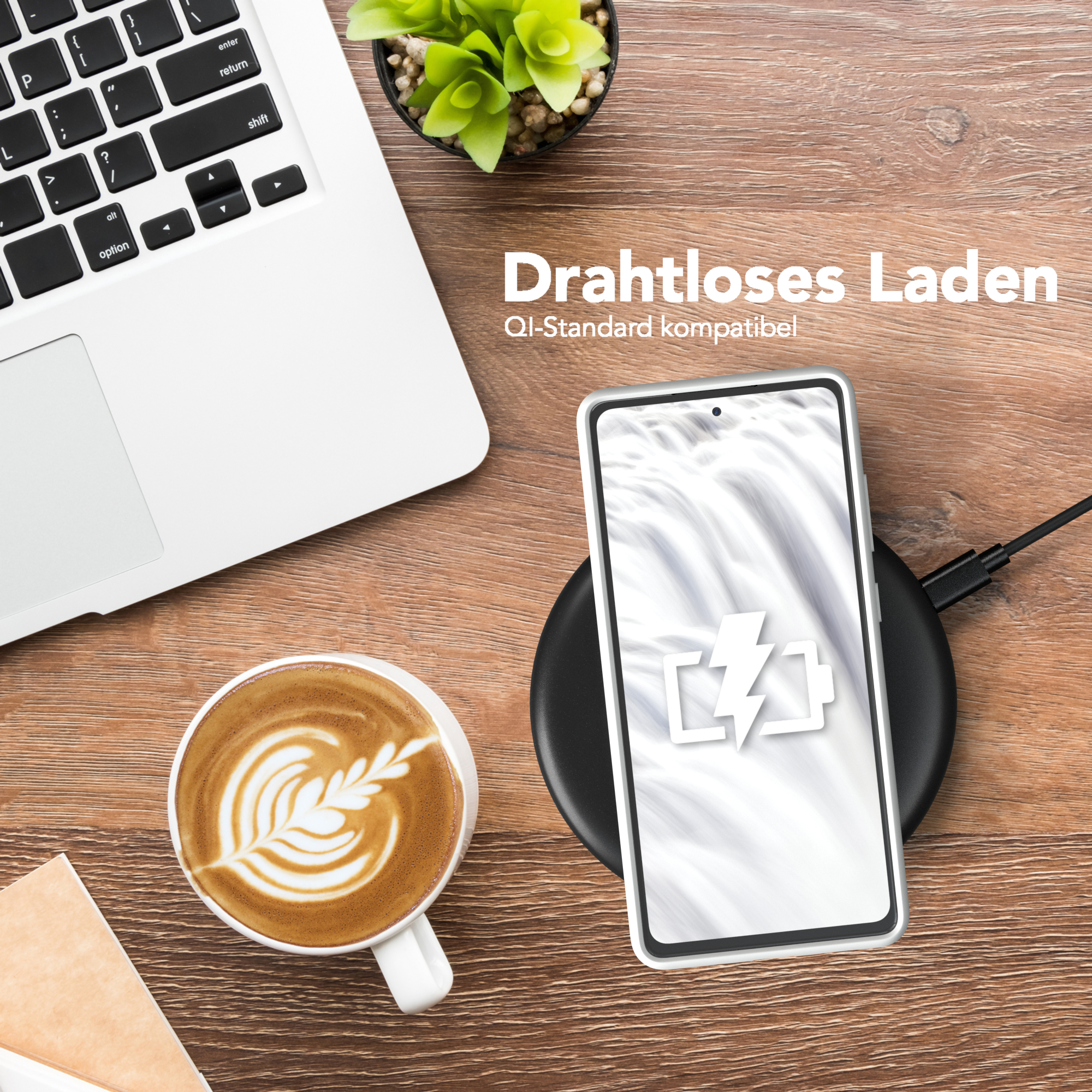 Handy lädt drahtlos auf Schreibtisch mit Kaffee, Laptop und Pflanze. Draufsicht.
