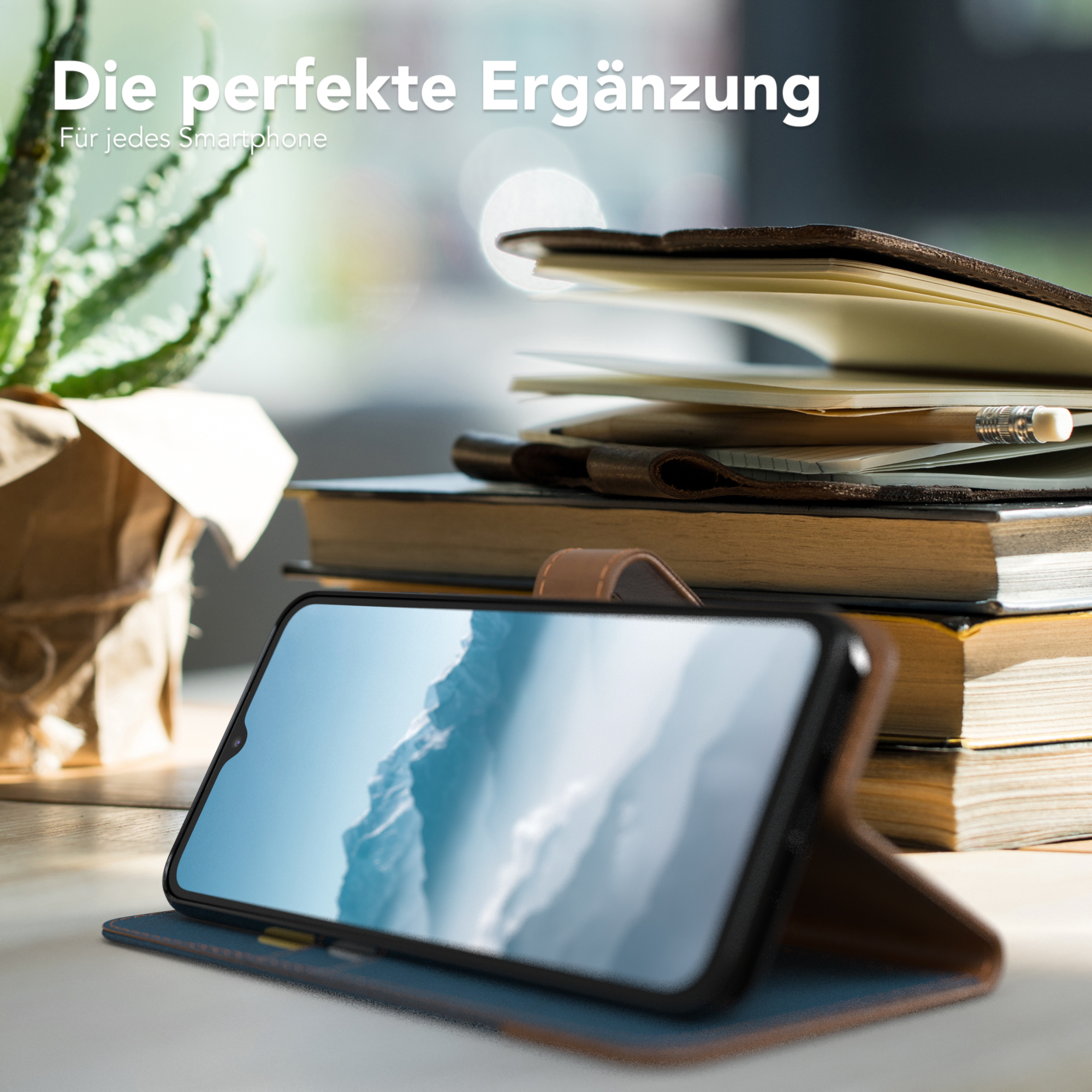 Smartphone in einer Hülle, lehnt an einem Stapel Bücher, im Hintergrund eine kleine Pflanze.