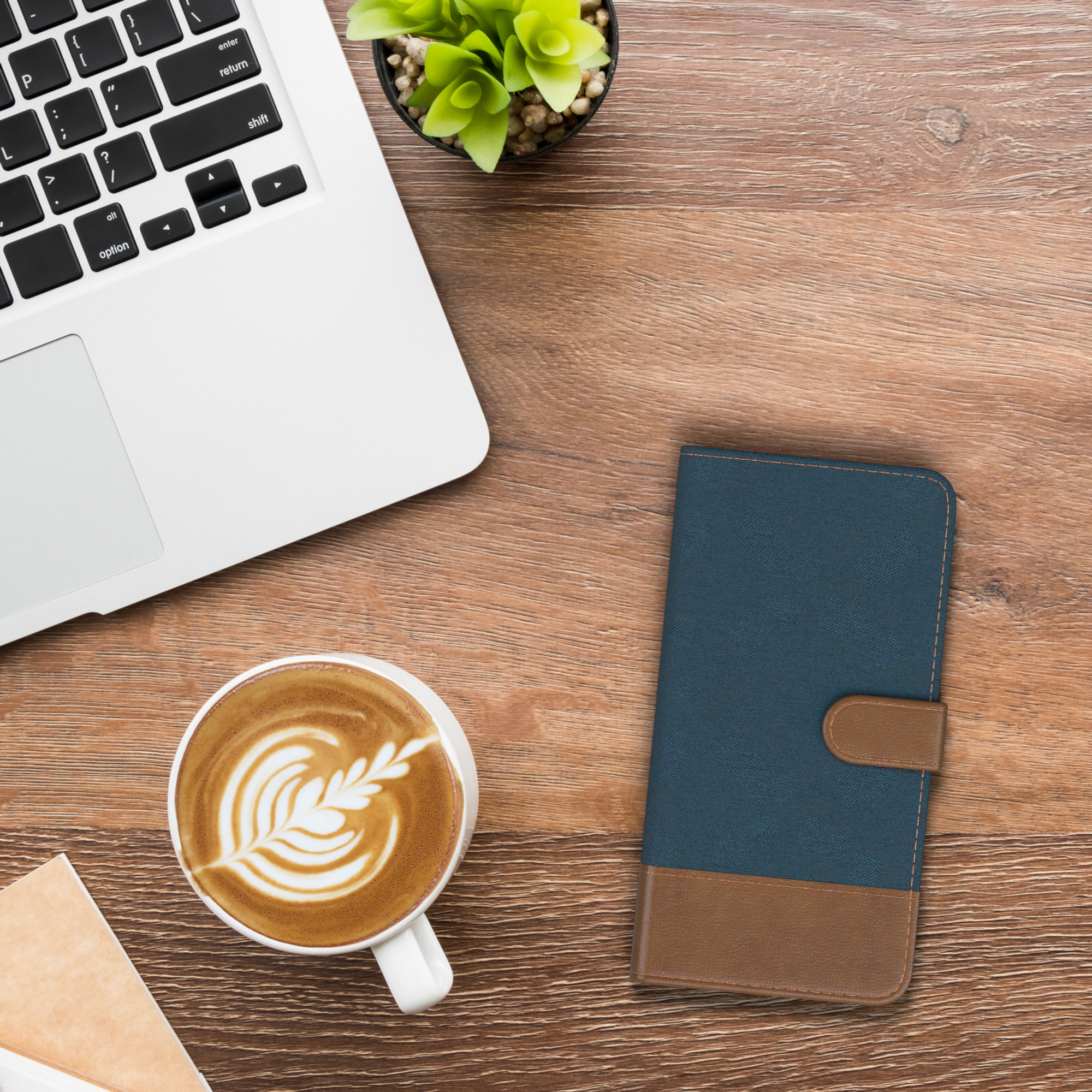 Ein Laptop, Kaffee mit Kunst und eine blau-braune Handyhülle auf einem Holztisch.