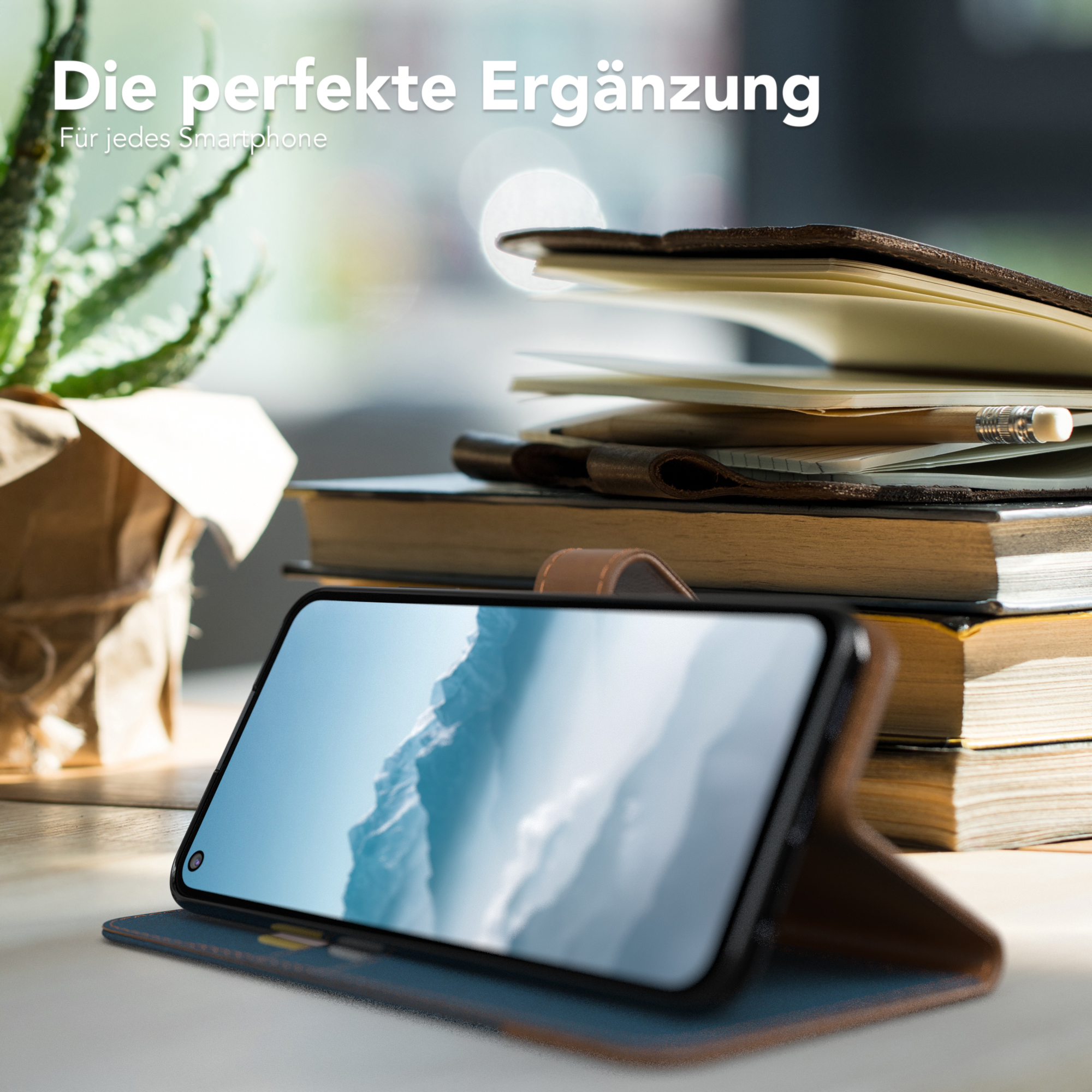 Telefon in einer Hülle, offen, auf einem Tisch mit Büchern und einer Pflanze.