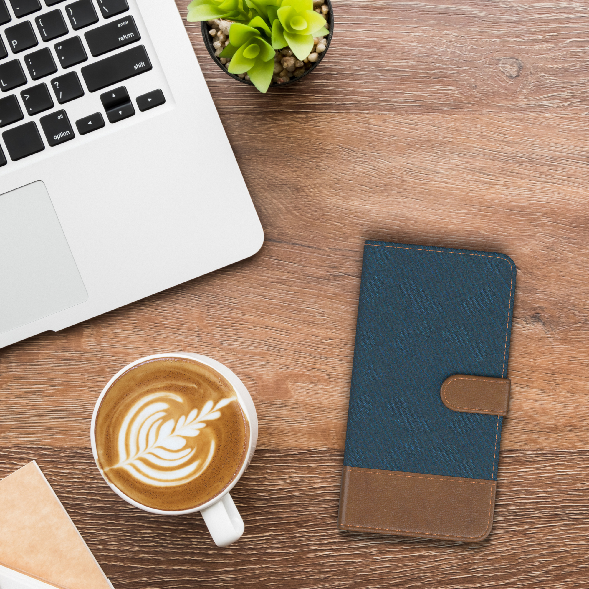 Draufsicht auf einen Schreibtisch mit Laptop, Kaffeetasse, Handyhülle und einer Pflanze.