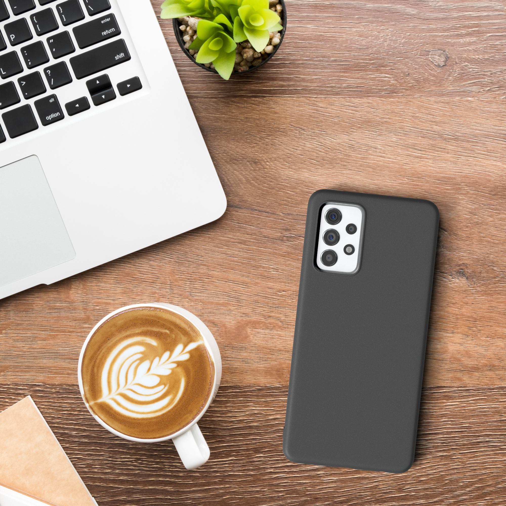 Laptop, Kaffee und eine Handyhülle auf einem hölzernen Schreibtisch.