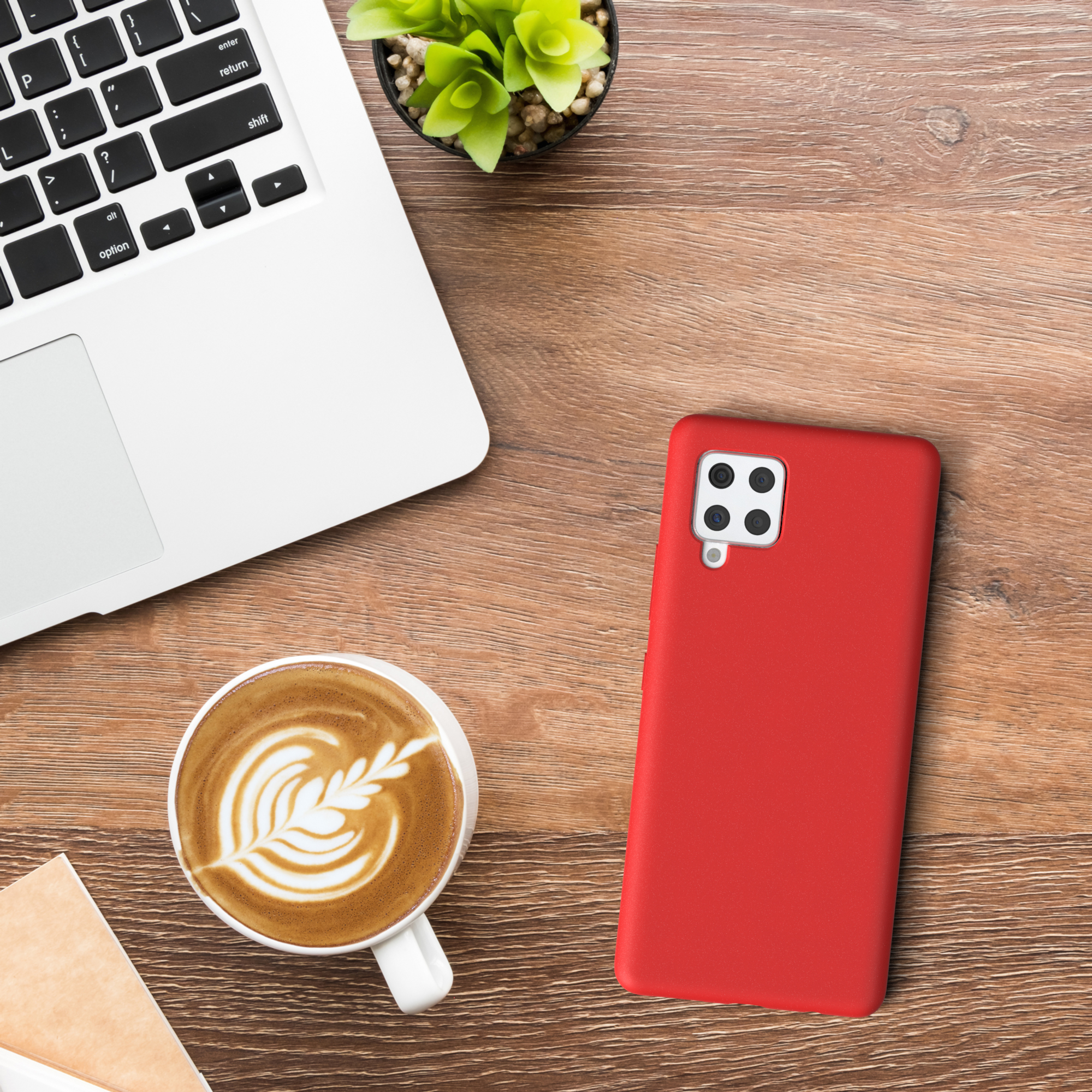 Eine rote Handyhülle und ein Laptop befinden sich auf einem Holzschreibtisch. Es gibt auch eine Tasse Kaffee und eine Pflanze.