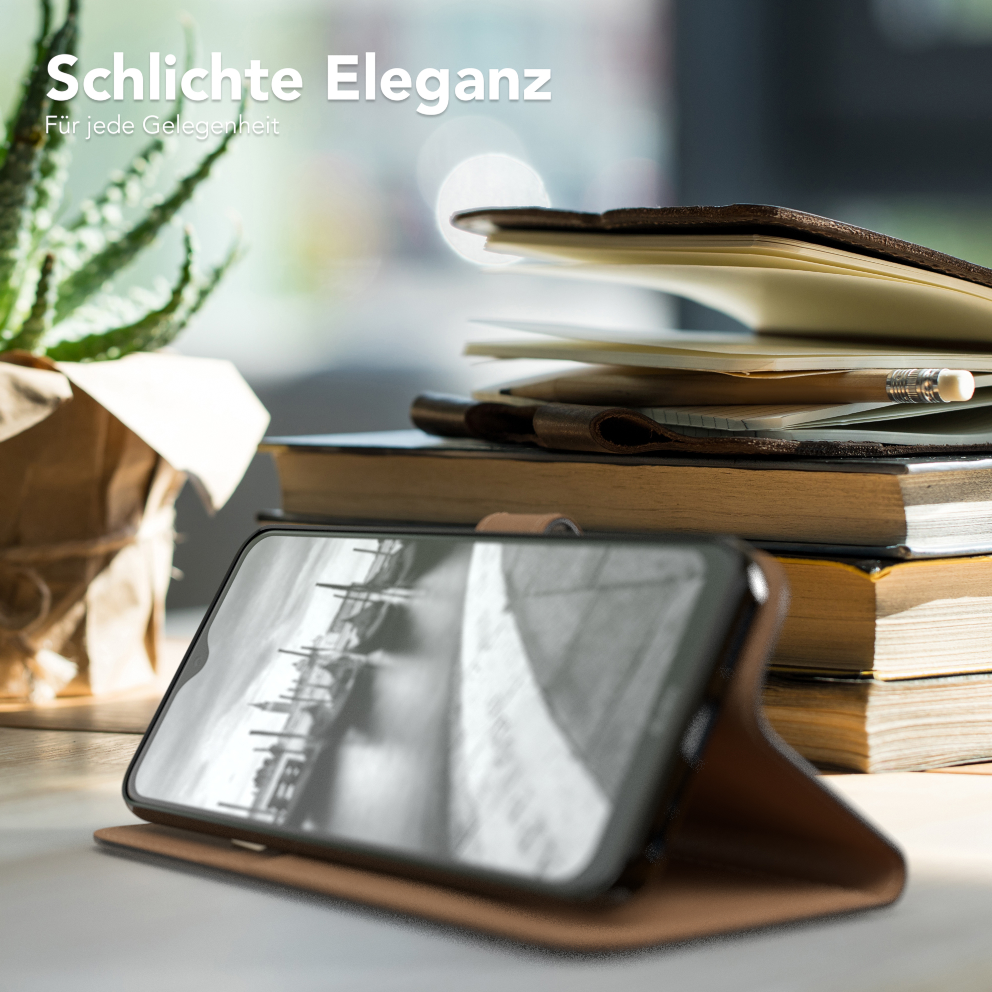 Telefon in einer braunen Lederhülle, offen auf einem Tisch mit Büchern und einer Pflanze. Natürliches Licht.