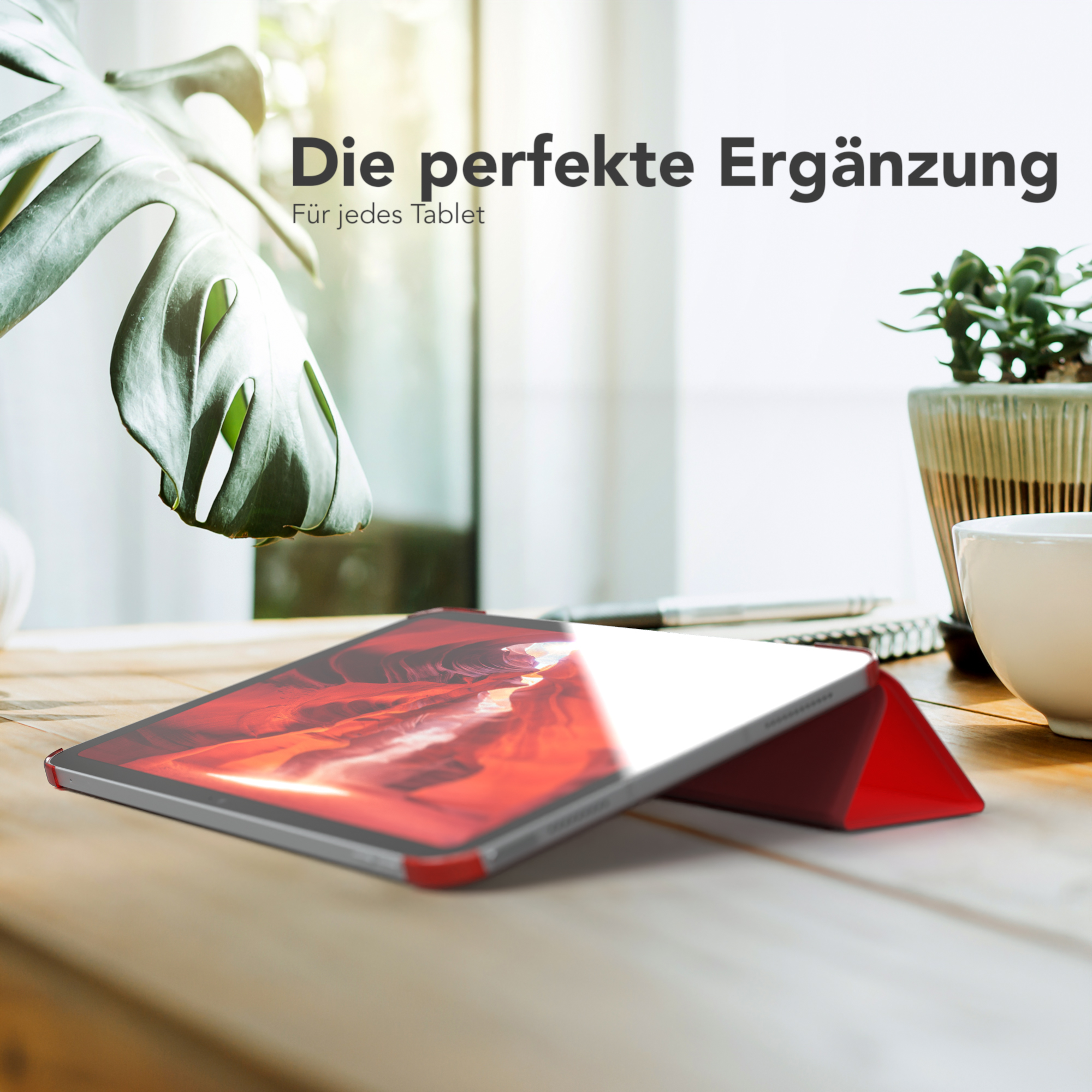 Tablet in roter Hülle auf einem Schreibtisch mit Pflanze, Tasse. Verschwommener Hintergrund.