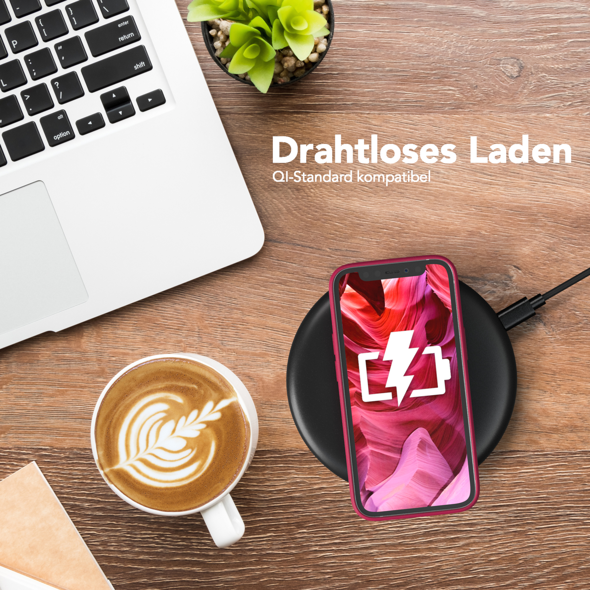Ein Telefon lädt auf einem schwarzen Pad, mit einer Latte Art Kaffeetasse und einem Laptop auf einem Schreibtisch.
