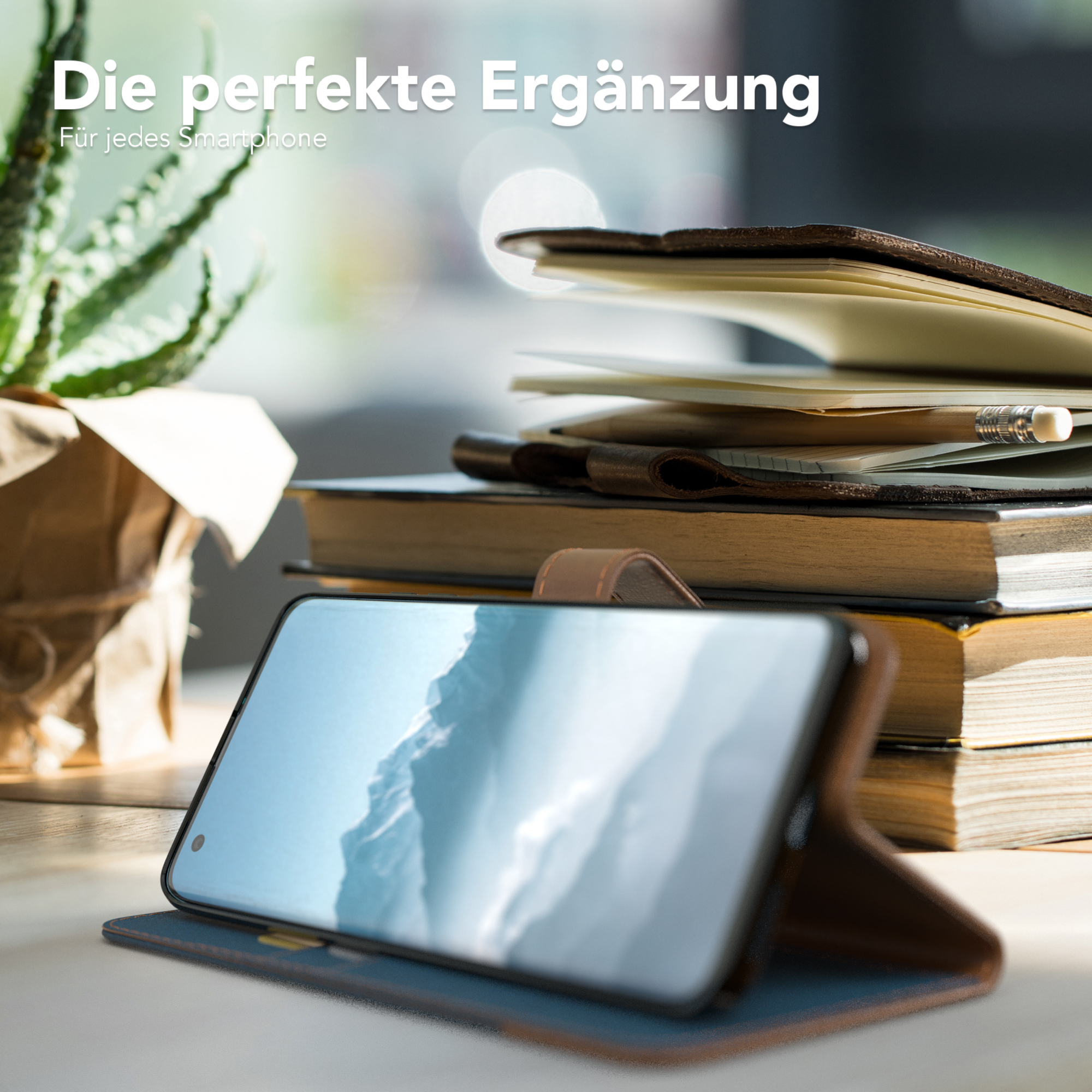 Telefon in Hülle, aufgestellt, Bücher und Pflanze im Hintergrund.