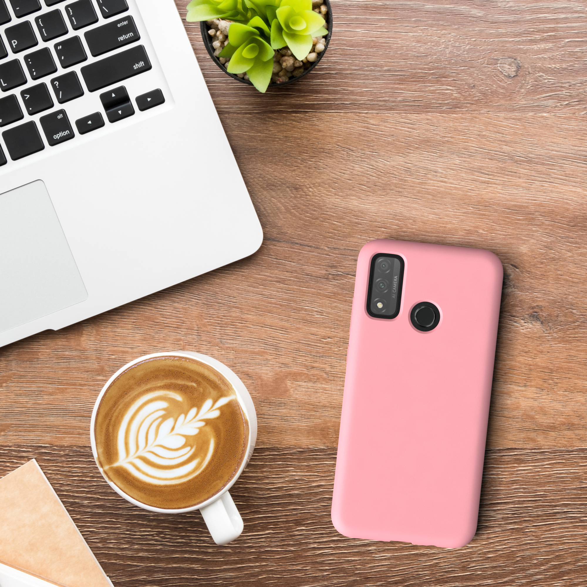 Ein Telefon in einer rosa Hülle und eine Tasse Kaffee auf einem Holztisch. Ein Laptop und eine Pflanze sind ebenfalls auf dem Tisch.