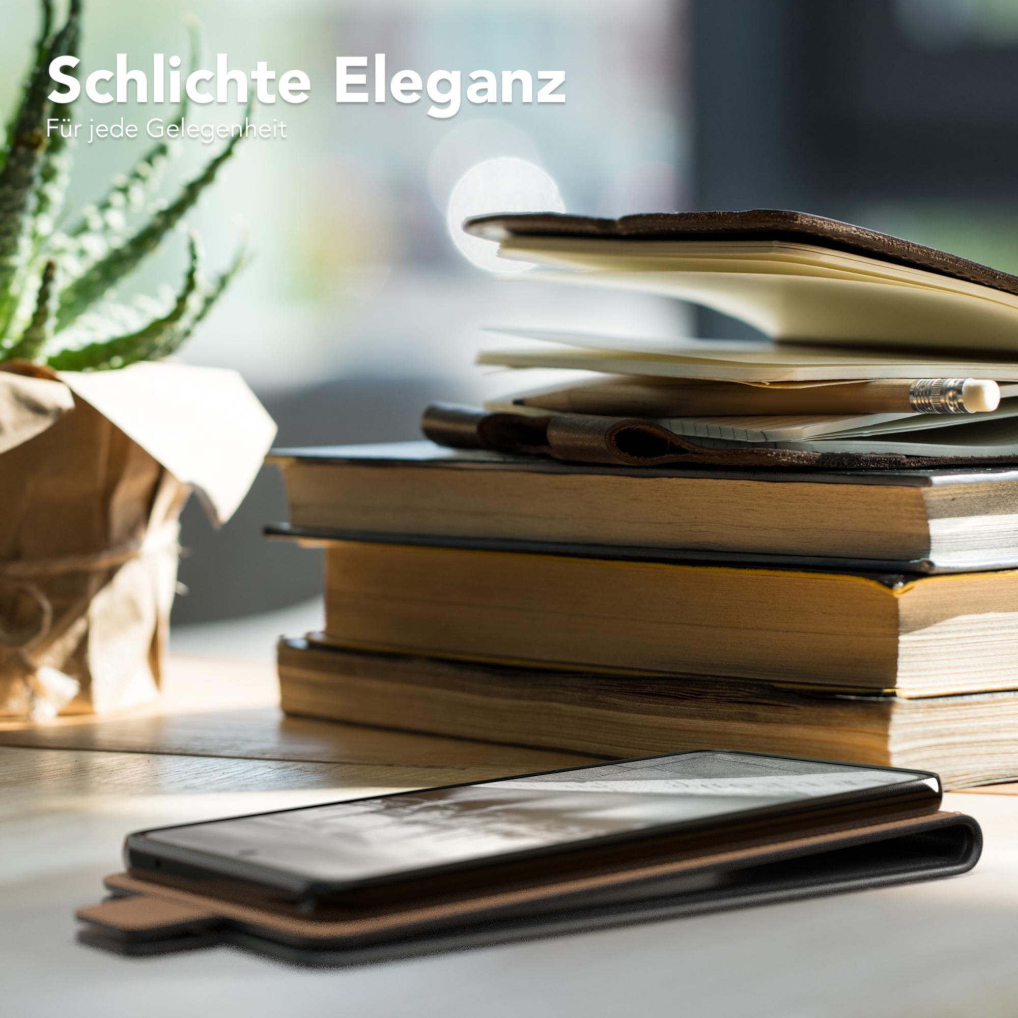 Ein Schreibtisch mit Handyhülle, Büchern, einer Pflanze und einem Laptop, mit unscharfem Hintergrund.