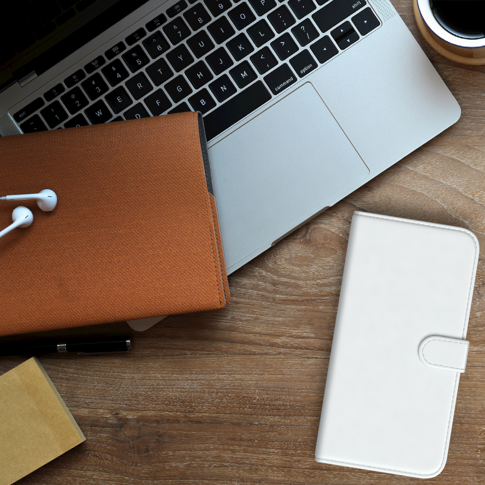 Laptop, Handyhülle und Zubehör auf einem Holztisch. Kopfhörer und Kaffeetasse sind ebenfalls sichtbar.