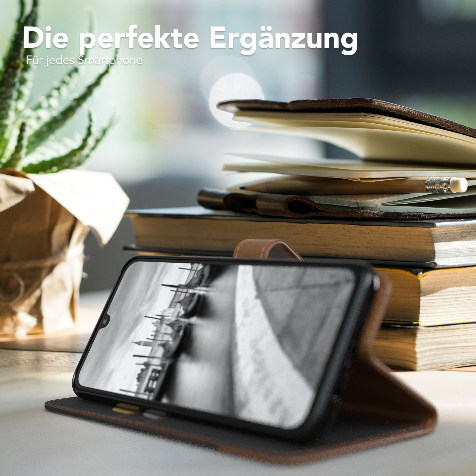 Ein Telefon in einer Hülle mit Landschaft. Geöffnet auf einem Schreibtisch mit Büchern und Pflanze.