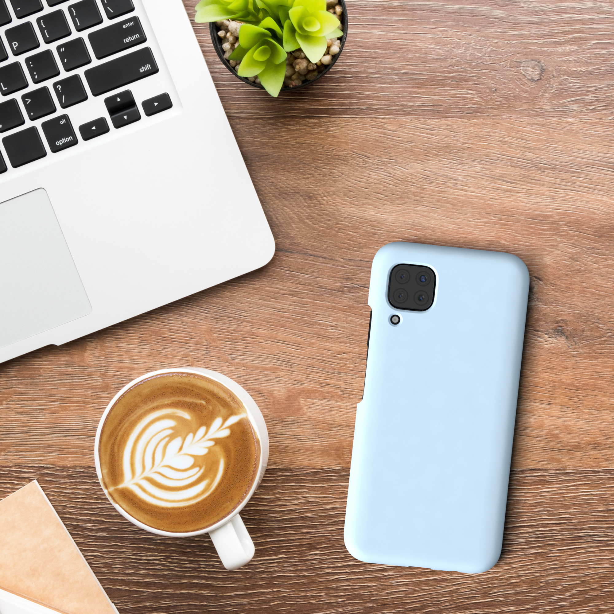 Ein Laptop, eine Tasse Kaffee mit Latte Art und eine hellblaue Handyhülle liegen auf einem Holztisch.