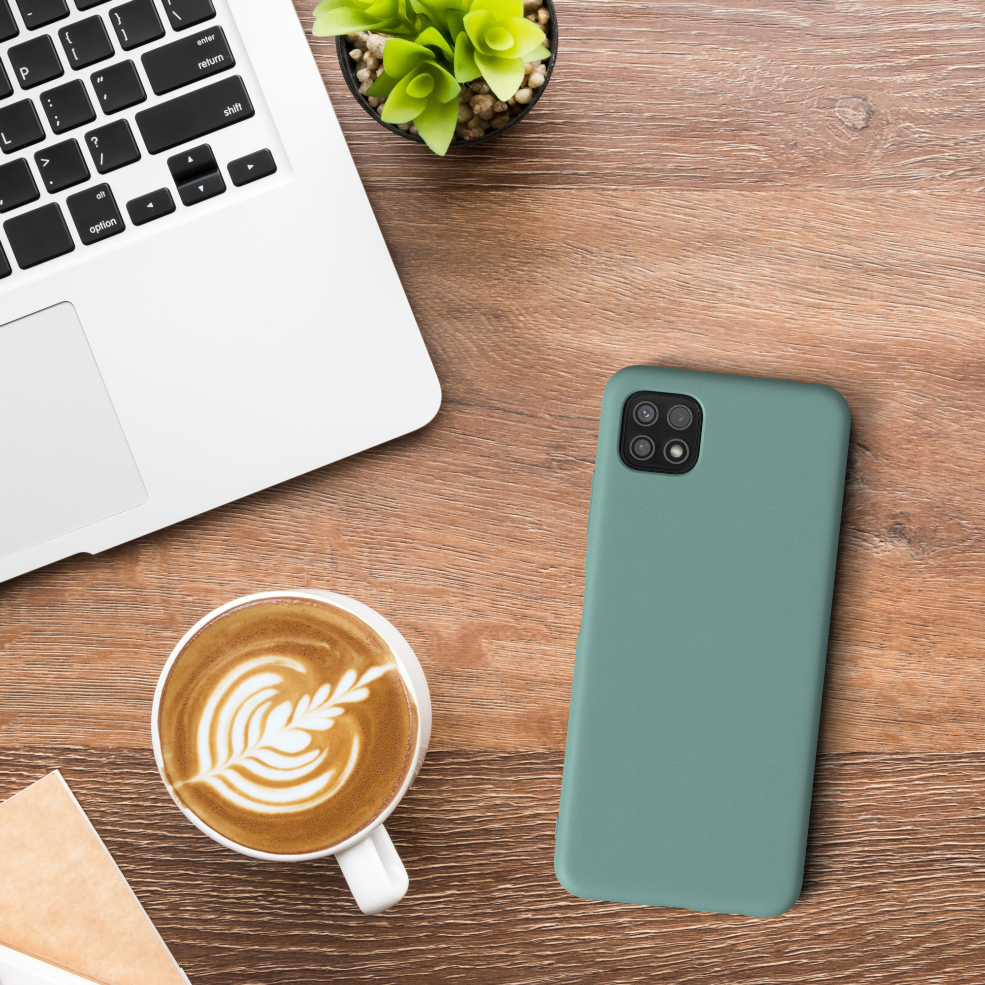 Draufsicht auf einen Schreibtisch mit Laptop, Kaffee, Telefon und Pflanze.