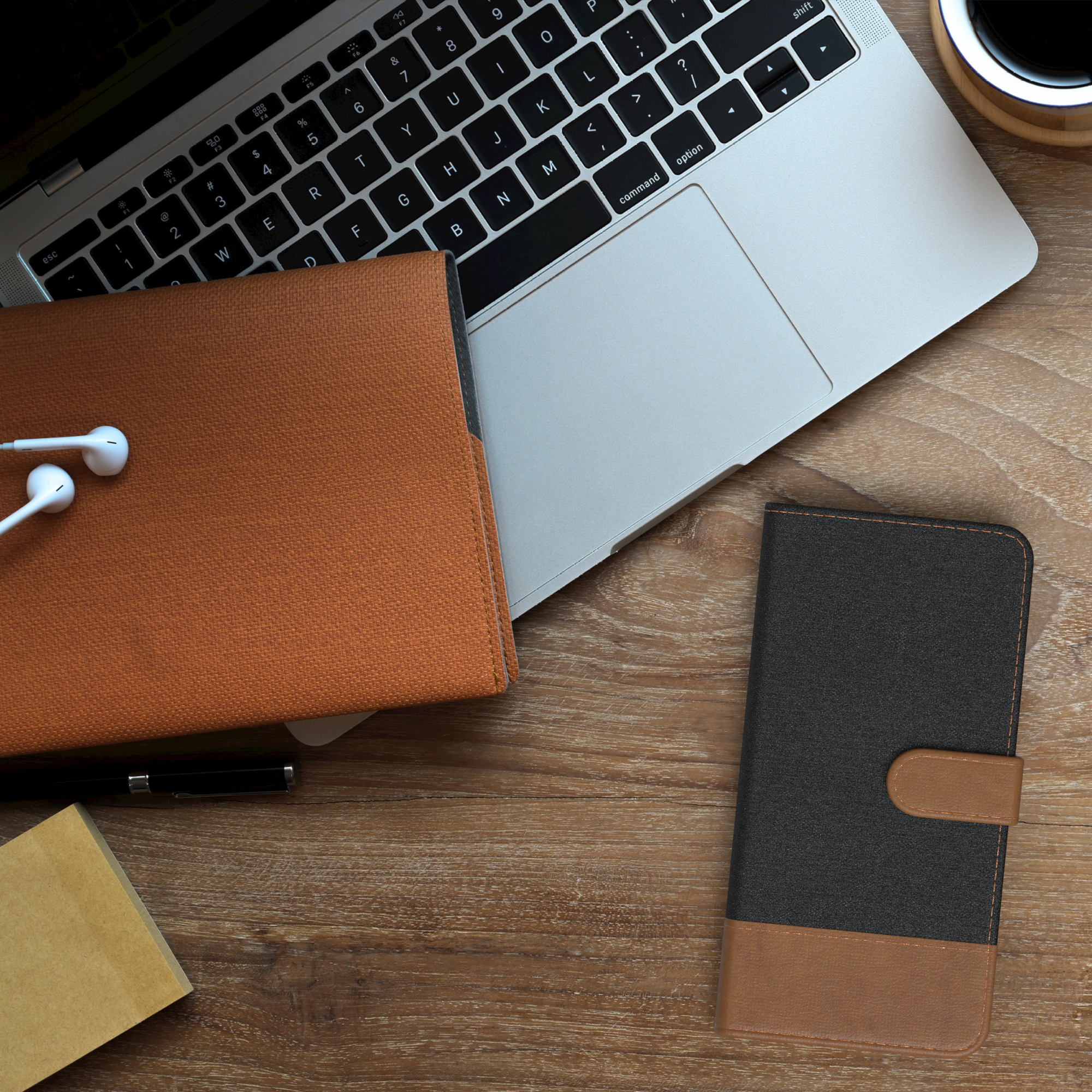 Laptop, offenes Notizbuch, Stift und Smartphone-Hülle auf einem Holzschreibtisch. Kaffeetasse und Ohrhörer vorhanden.