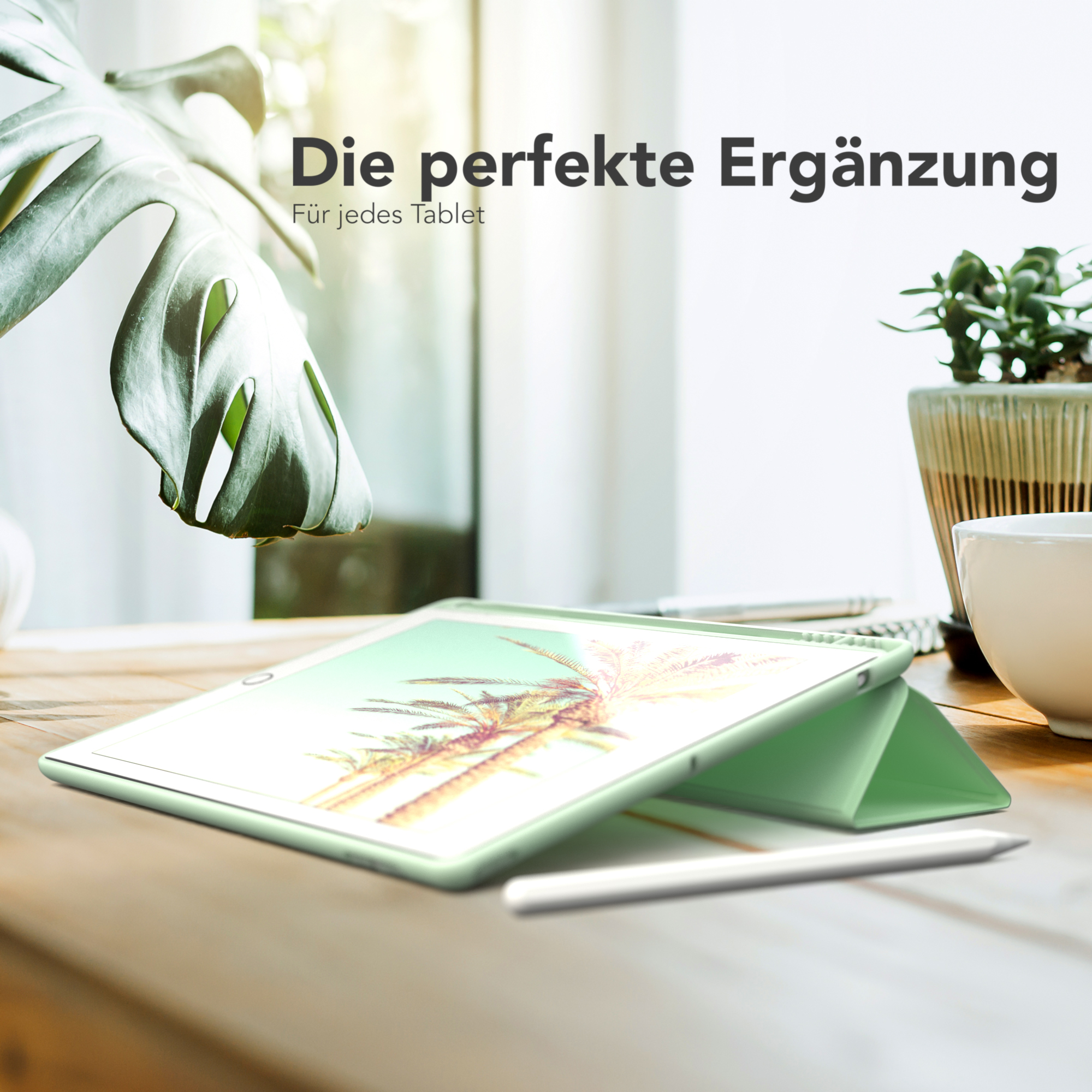 Ein grünes Tablet in einer grünen Hülle auf einem Holztisch, neben einem Stift und einer Pflanze. Text: 'Die perfekte Ergänzung'.