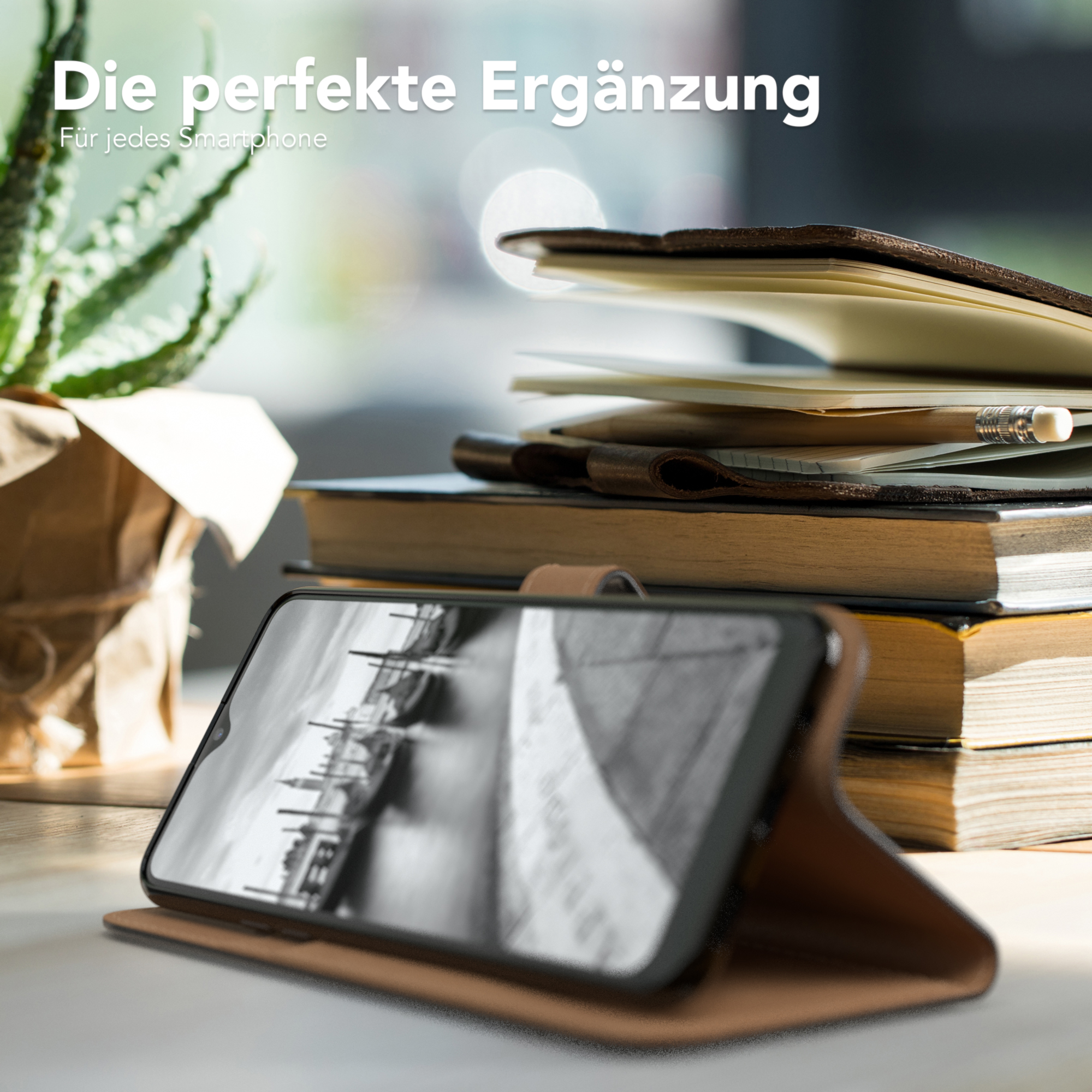 Telefon in einer Hülle, auf einem Tisch mit Büchern und einer Pflanze. Schwarz-Weiß-Bild auf dem Bildschirm.
