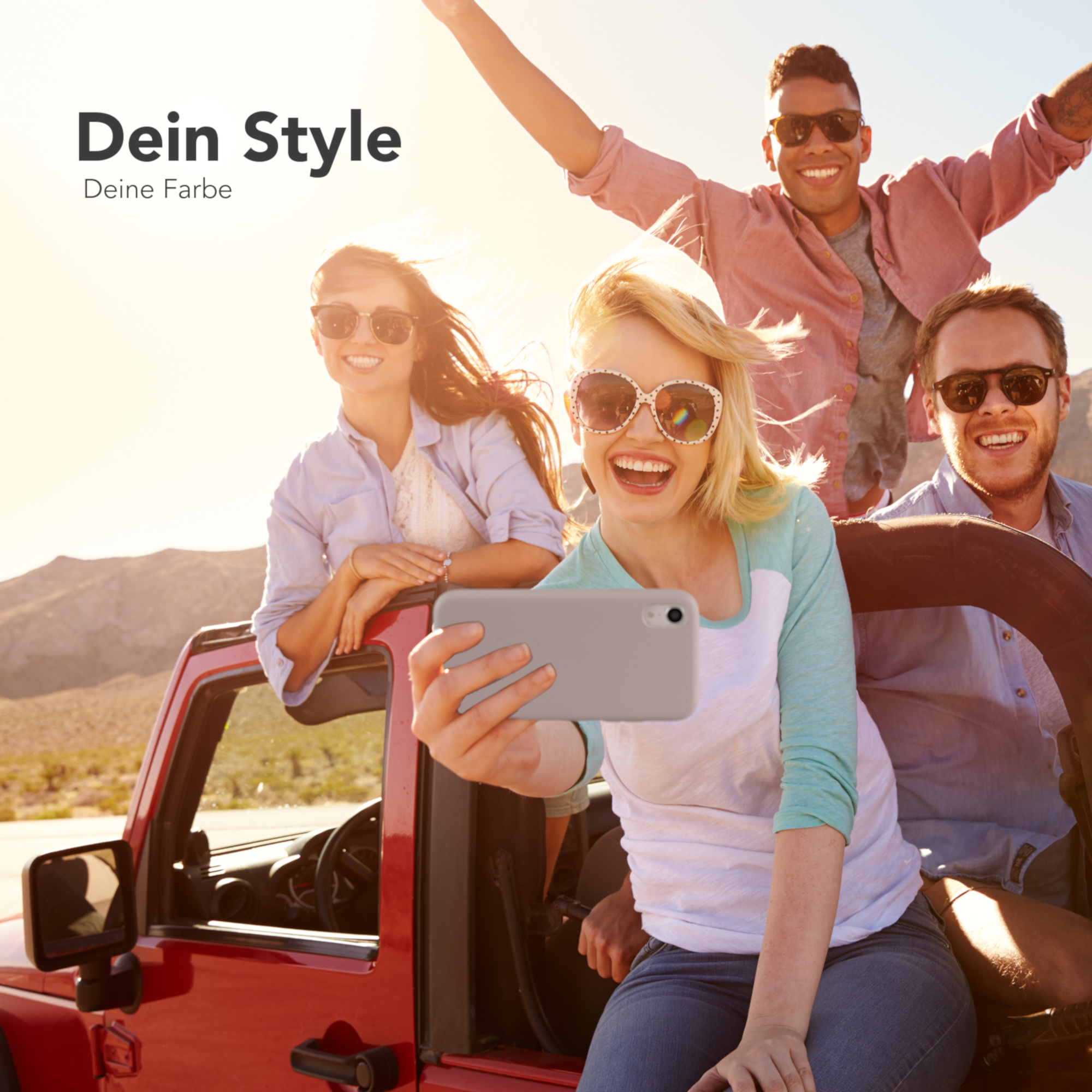 Vier Personen in einem roten Jeep machen ein Selfie. Die Frau mit dem Telefon lächelt in die Kamera. Der Hintergrund ist sonnig.