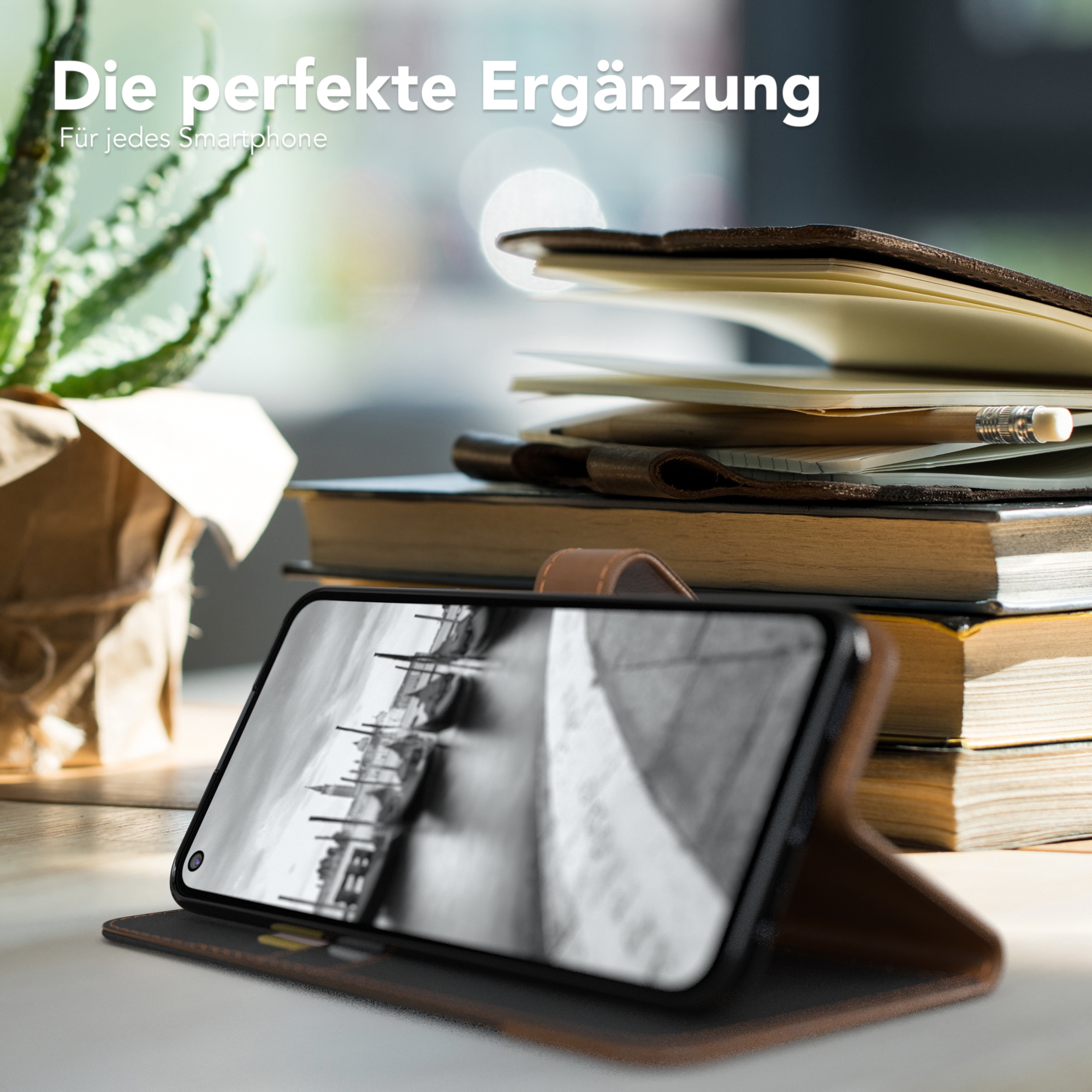 Telefon in einer Hülle auf einem Tisch mit Büchern und einer Pflanze. Text: Die perfekte Ergänzung.