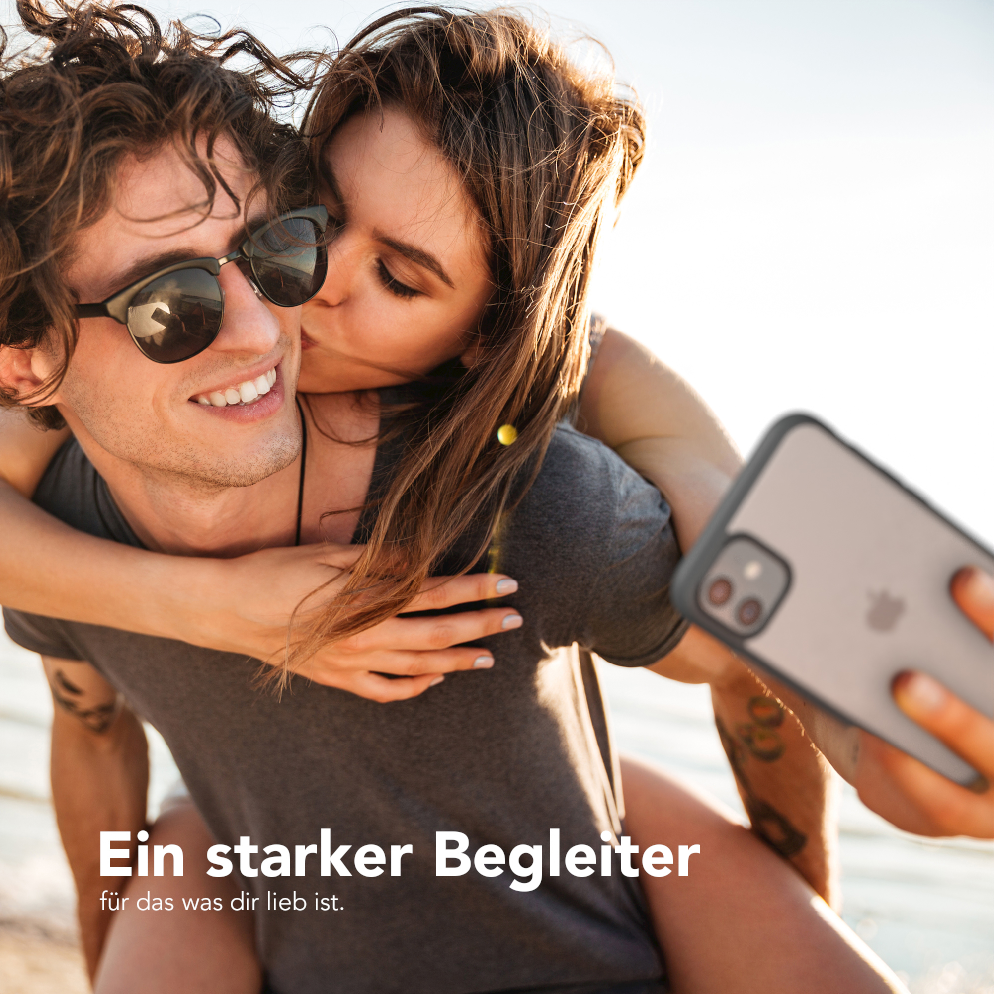 Paar macht Selfie. Frau küsst Mann. Hintergrund ist Strand und Sonnenlicht.